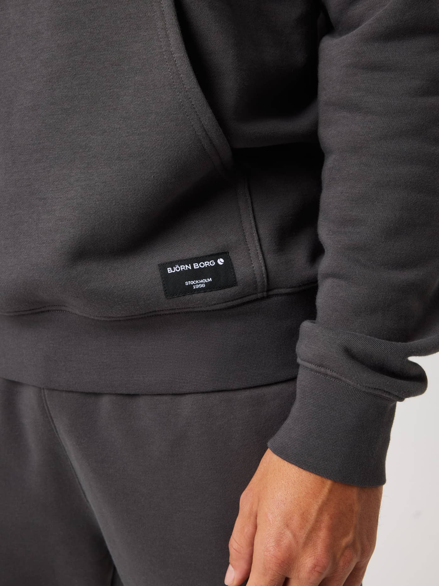Close-up of the Björn Borg Centre Hoodie in Asphalt (Grey) featuring the black woven logo label on the hip. - Image 4