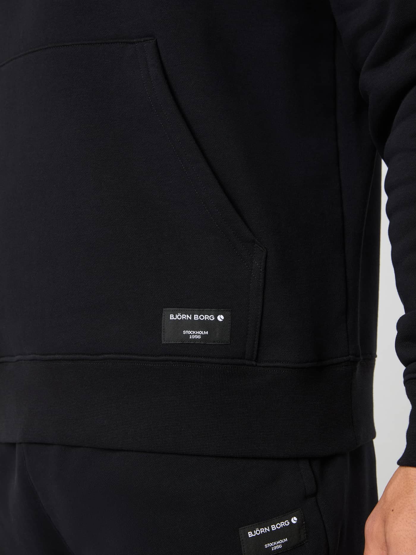 Detail van de Centre Hoodie voor heren in Black Beauty (Zwart) met kangoeroezak en wit geweven Björn Borg-logolabel. - Image 4