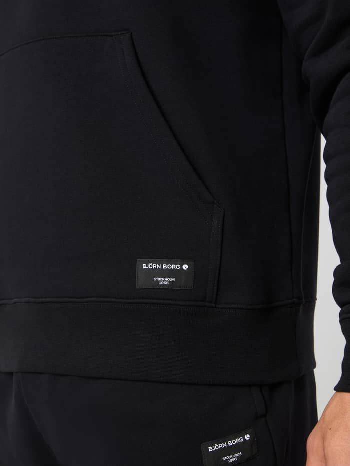 Detail van de Centre Hoodie voor heren in Black Beauty (Zwart) met kangoeroezak en wit geweven Björn Borg-logolabel. - Image 4