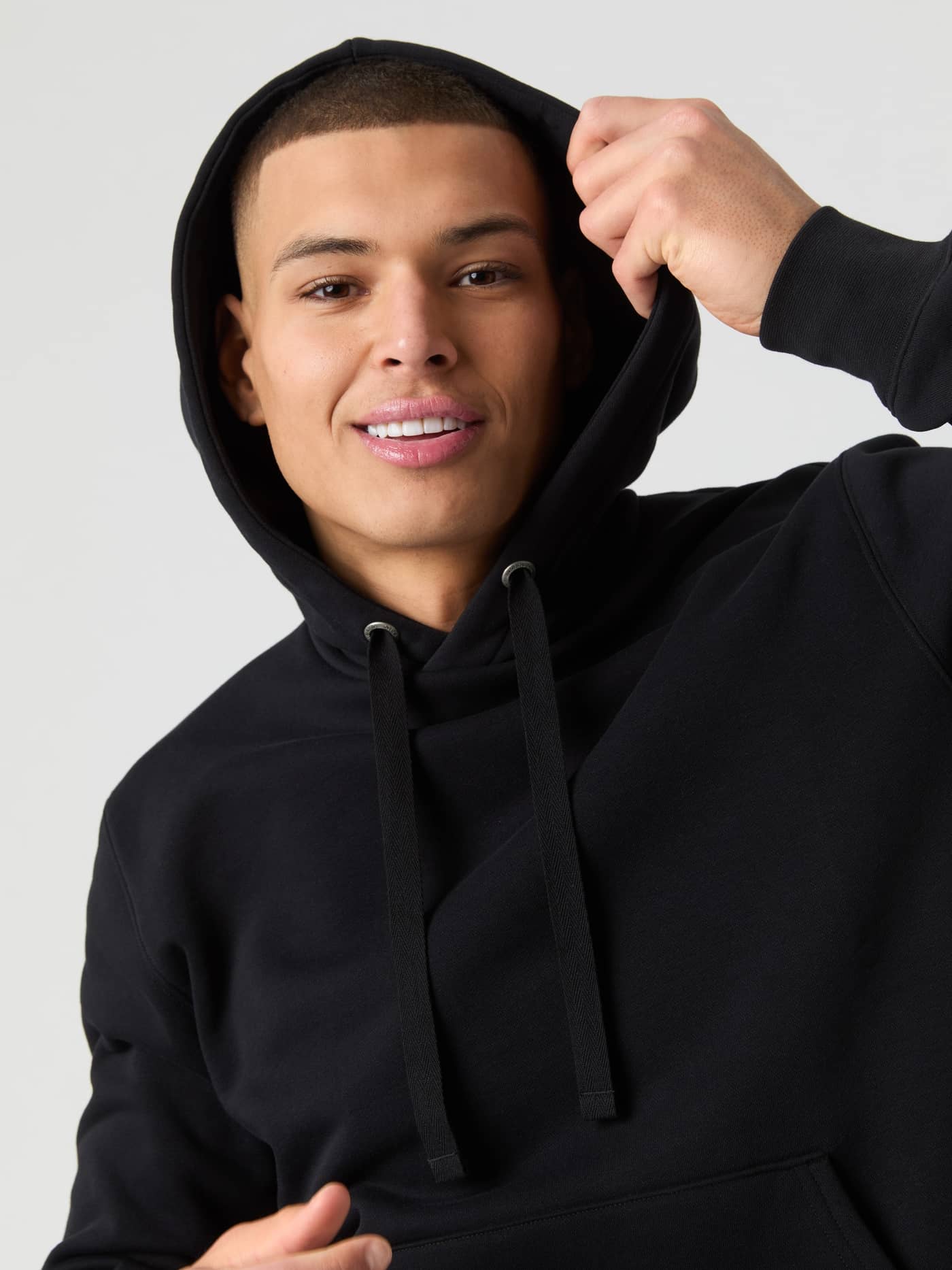 Close-up van een man in de Björn Borg Centre Hoodie in Black Beauty (Zwart), glimlachend terwijl hij de capuchon opzet. - Image 5