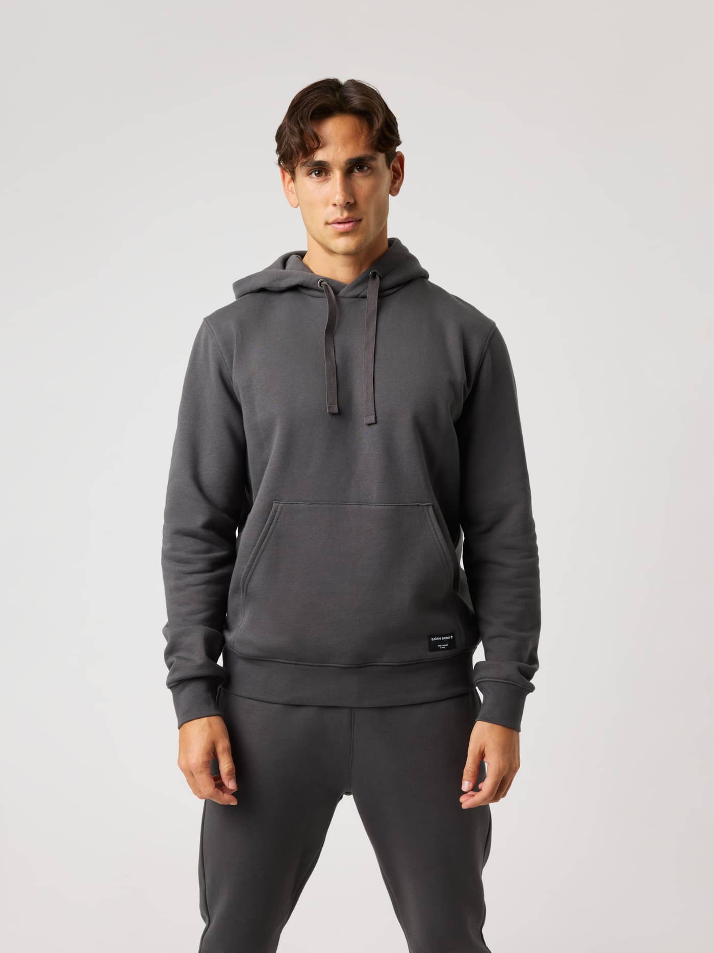 Vue de face d'un modèle portant le Centre Hoodie Asphalt (Gris) avec poche kangourou et capuche à cordons. - Image 1