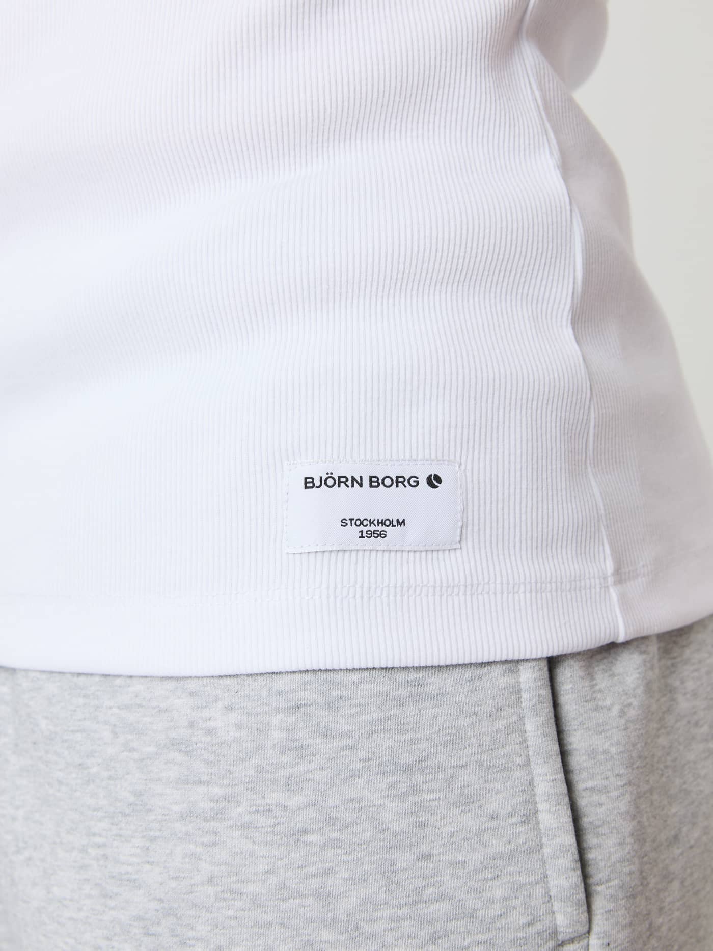 Close-up van de slim-fit Centre Ribbed Tank in Brilliant White (Wit) van geribde stof en een logolabel met zwarte tekst. - Image 4