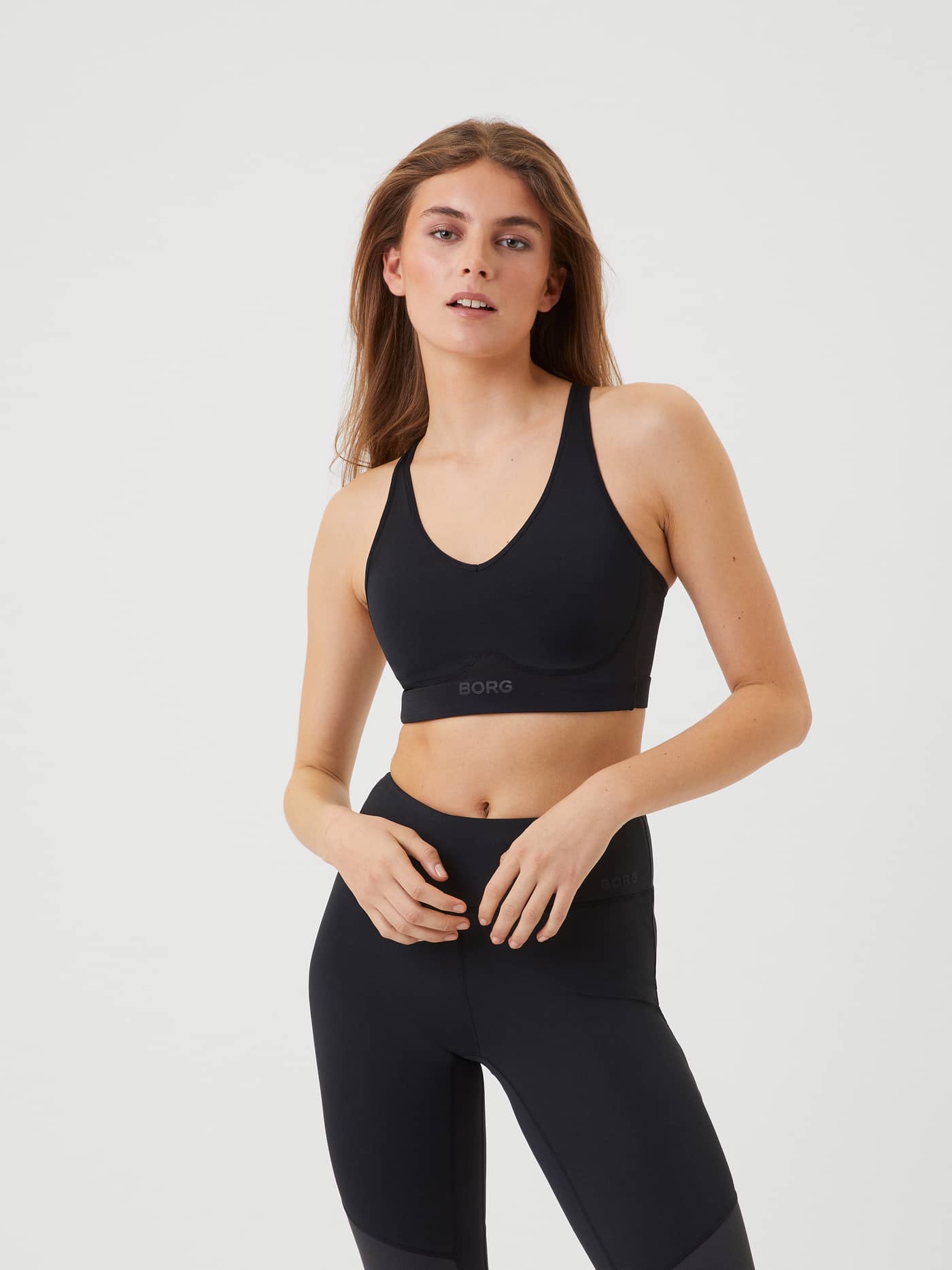 Vue de face d'un mannequin portant le Borg Mid V Support Sports Bra Noir, col en V et logo ton sur ton pour l'entraînement. - Image 2