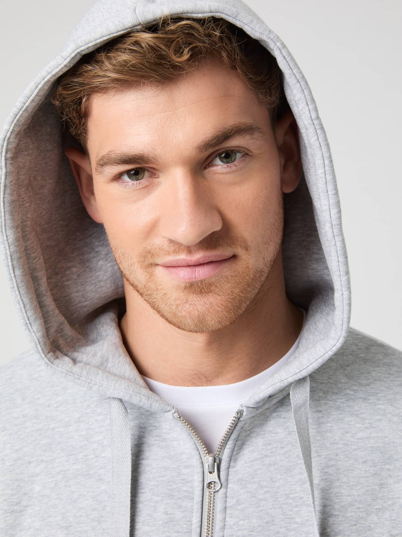 Close-up of a man in the functional cotton-blend Björn Borg Centre Zip Hoodie in Light Grey Melange (Grey) with the hood up. - Image 1