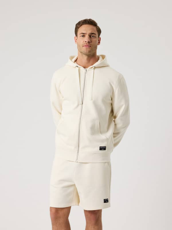 Vue de face d'un homme portant le Centre Zip Hoodie en Tofu (Blanc), un sweat à capuche zippé alliant style et fonction.