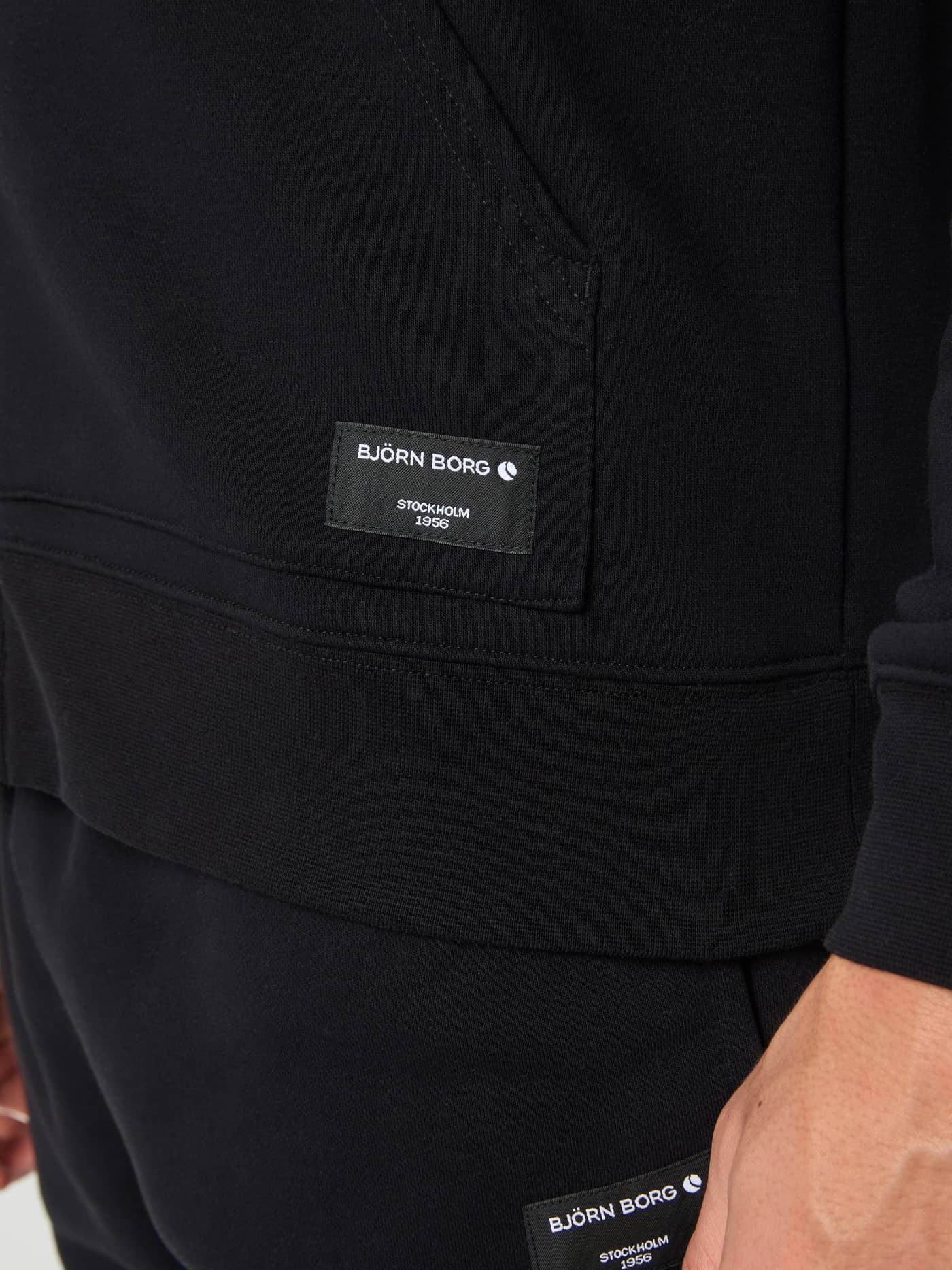 Close-up van het witte geweven logolabel op de Björn Borg Centre Zip Hoodie in Black Beauty (Zwart). - Image 4