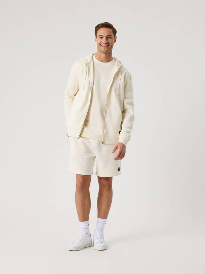 Full-body view of a man in the Björn Borg Centre Zip Hoodie in Tofu (White), featuring a functional zip and black logo. - Image 3