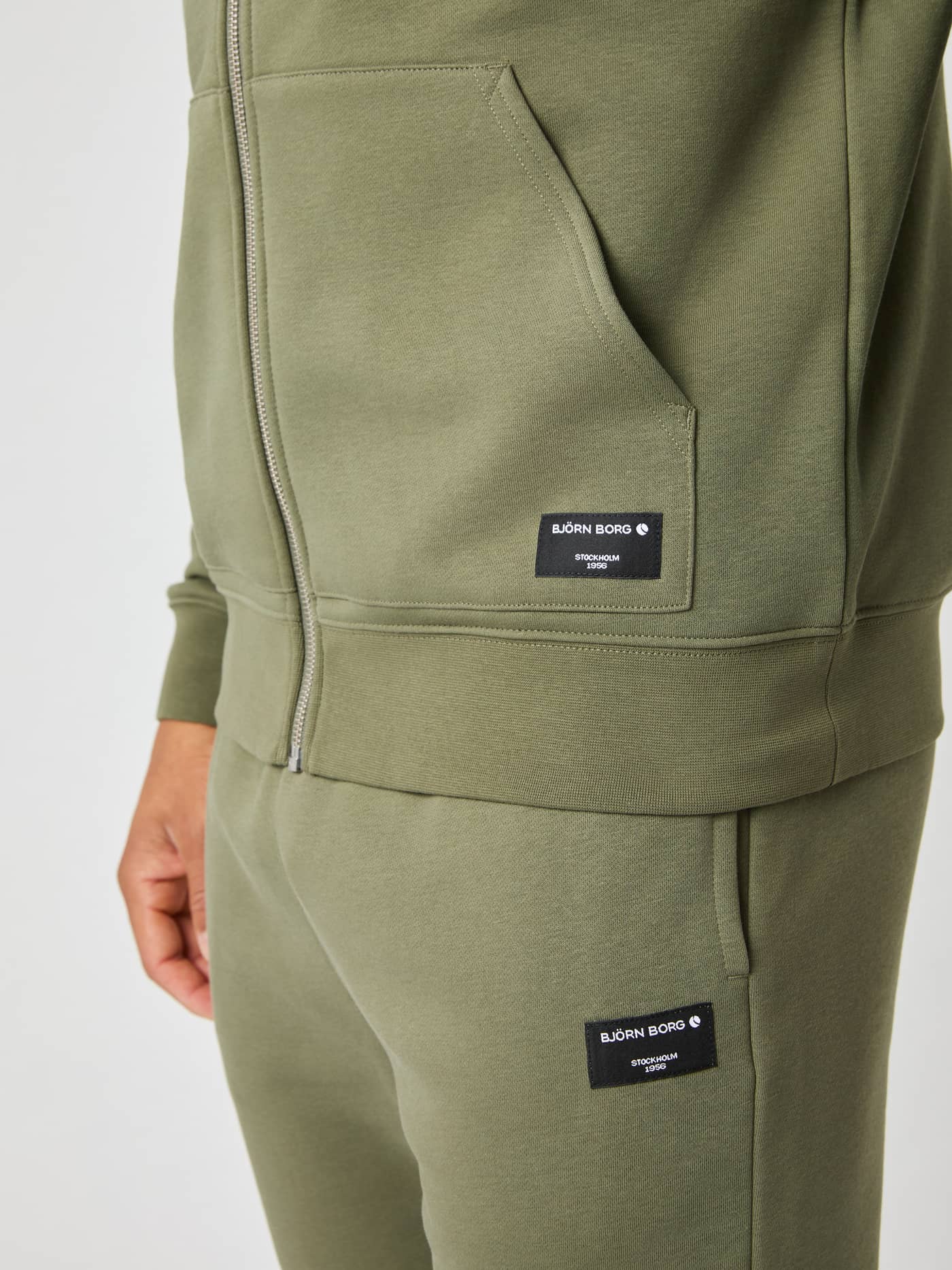 Nahaufnahme des Björn Borg Centre Zip Hoodie in Dusty Olive (Grün) mit schwarzem gewebtem Logo-Etikett auf der Fronttasche. - Image 5