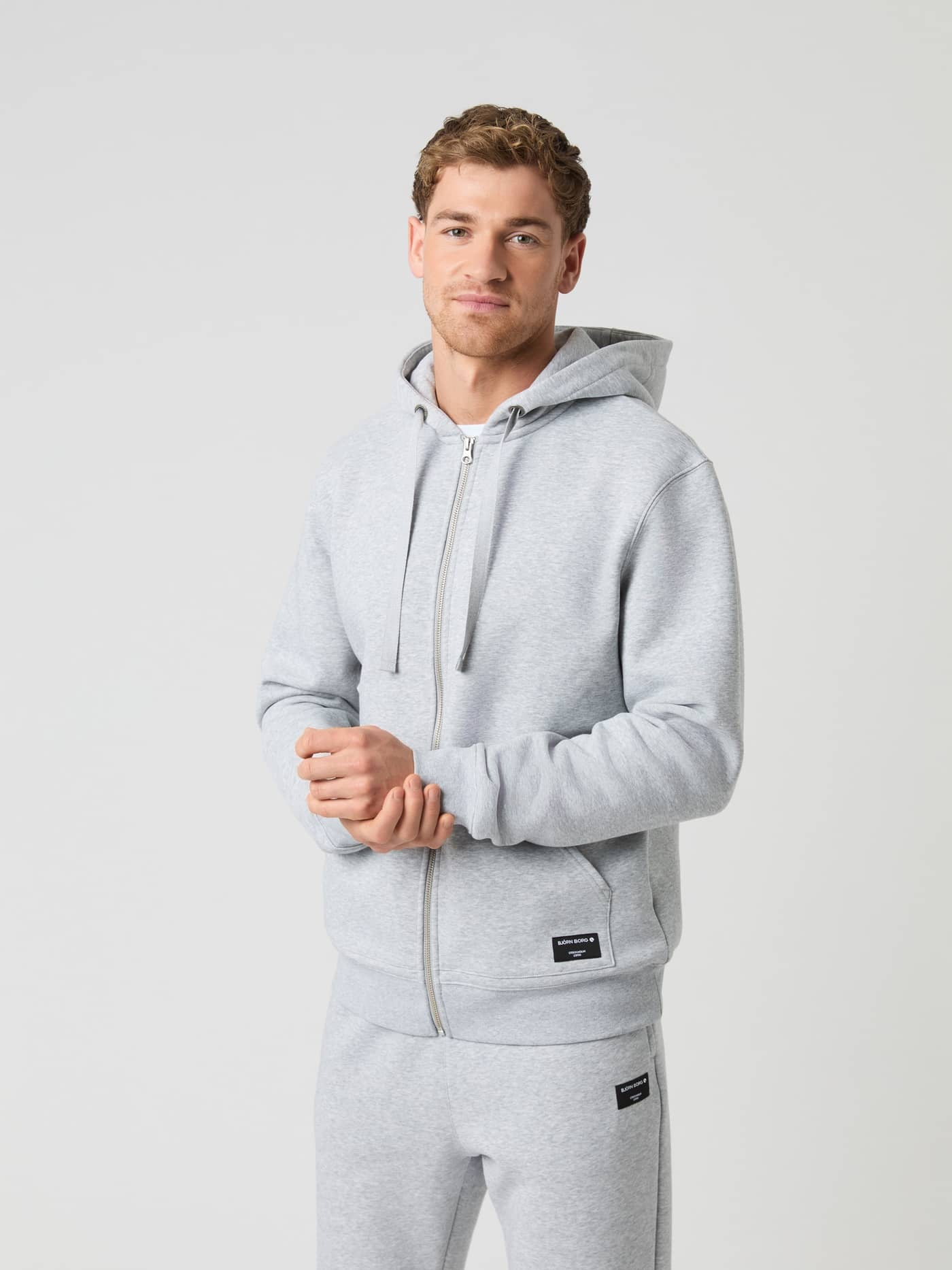 Vue de face d'un homme portant le Centre Zip Hoodie en Light Grey Melange (Gris) avec une fermeture éclair intégrale. - Image 1