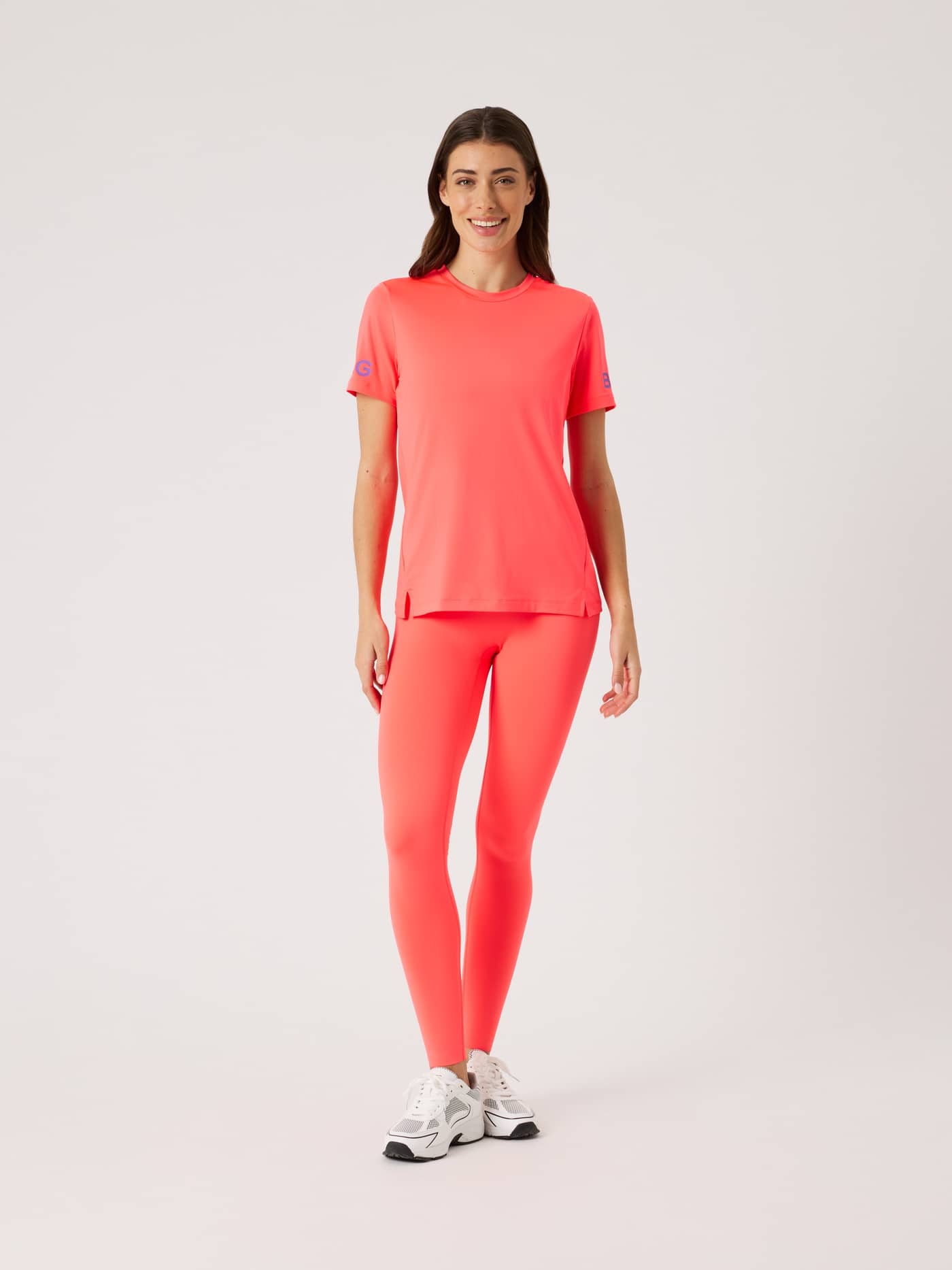 Full-body front view of a woman in the training Borg T-Shirt in Diva Pink (Pink) with side slits and blue arm logos. - Image 2