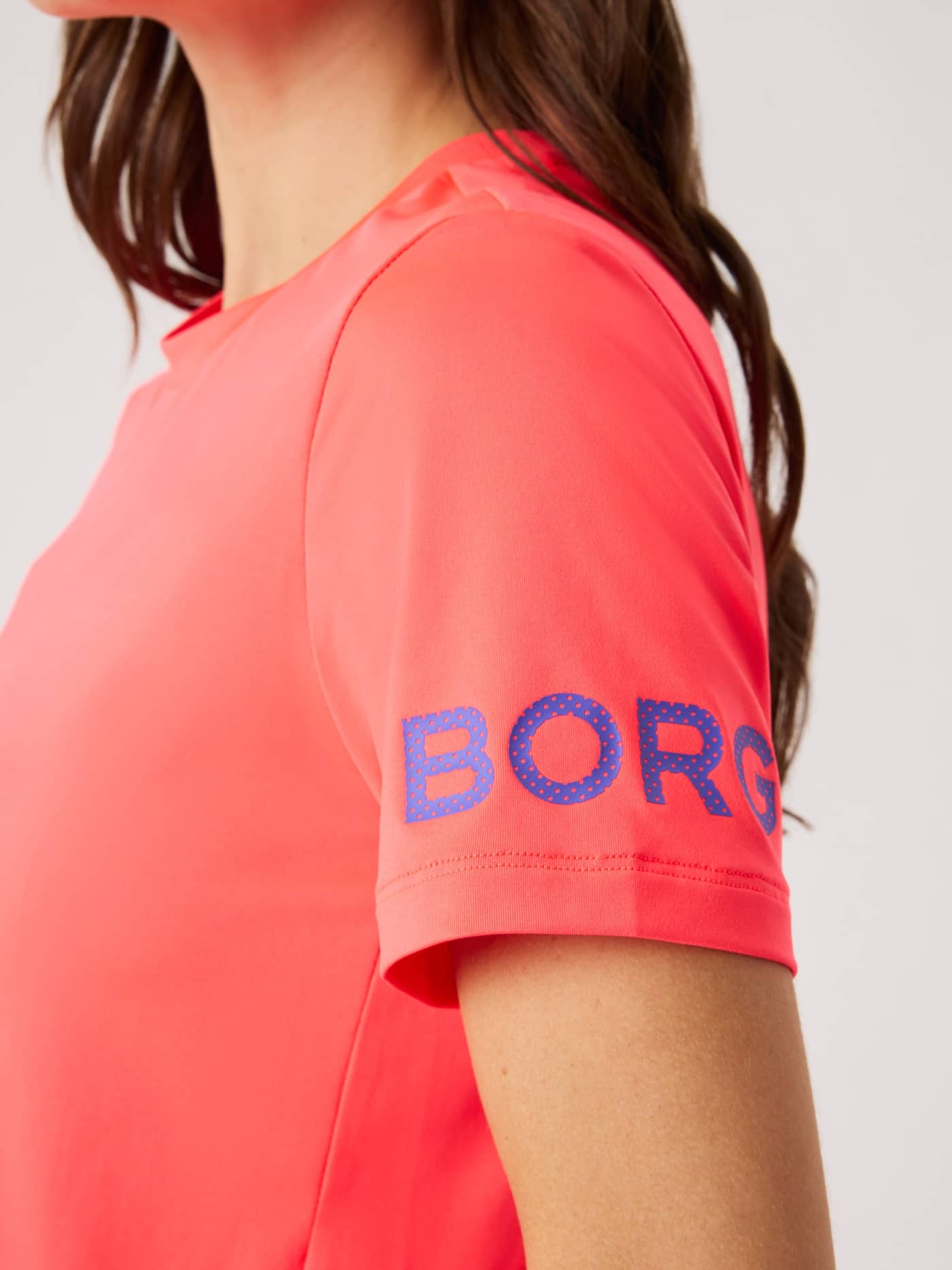 Detailed close-up of the purple logo on the sleeve of the Diva Pink (Pink) training Borg T-Shirt. - Image 5