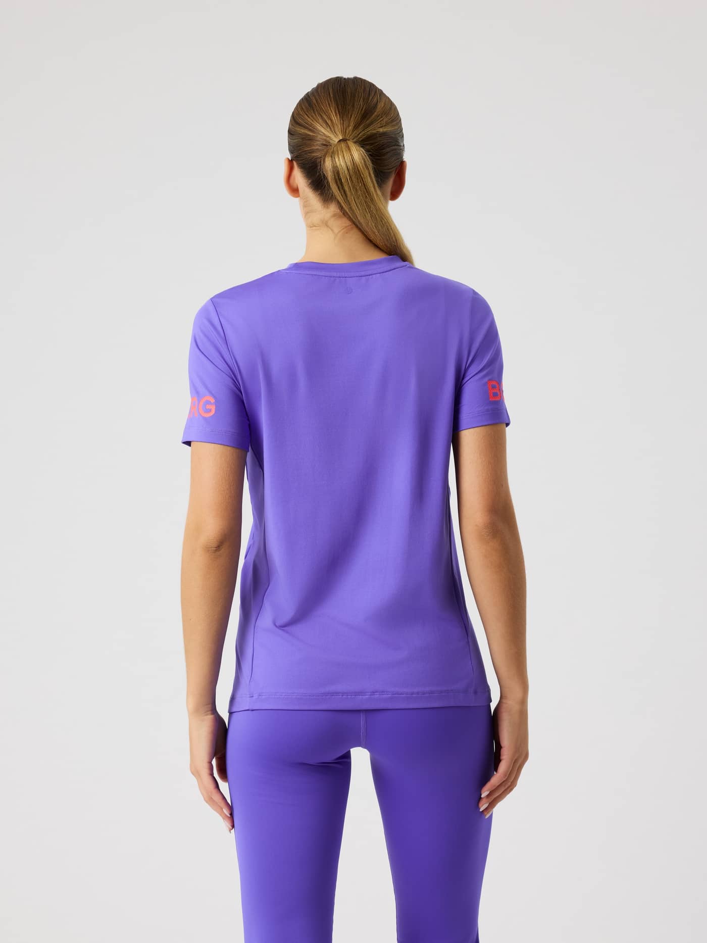 Vy bakifrån på en kvinna i Borg T-Shirt för träning i Simply Purple (Lila) med orangea logotyper och regular fit. - Image 2