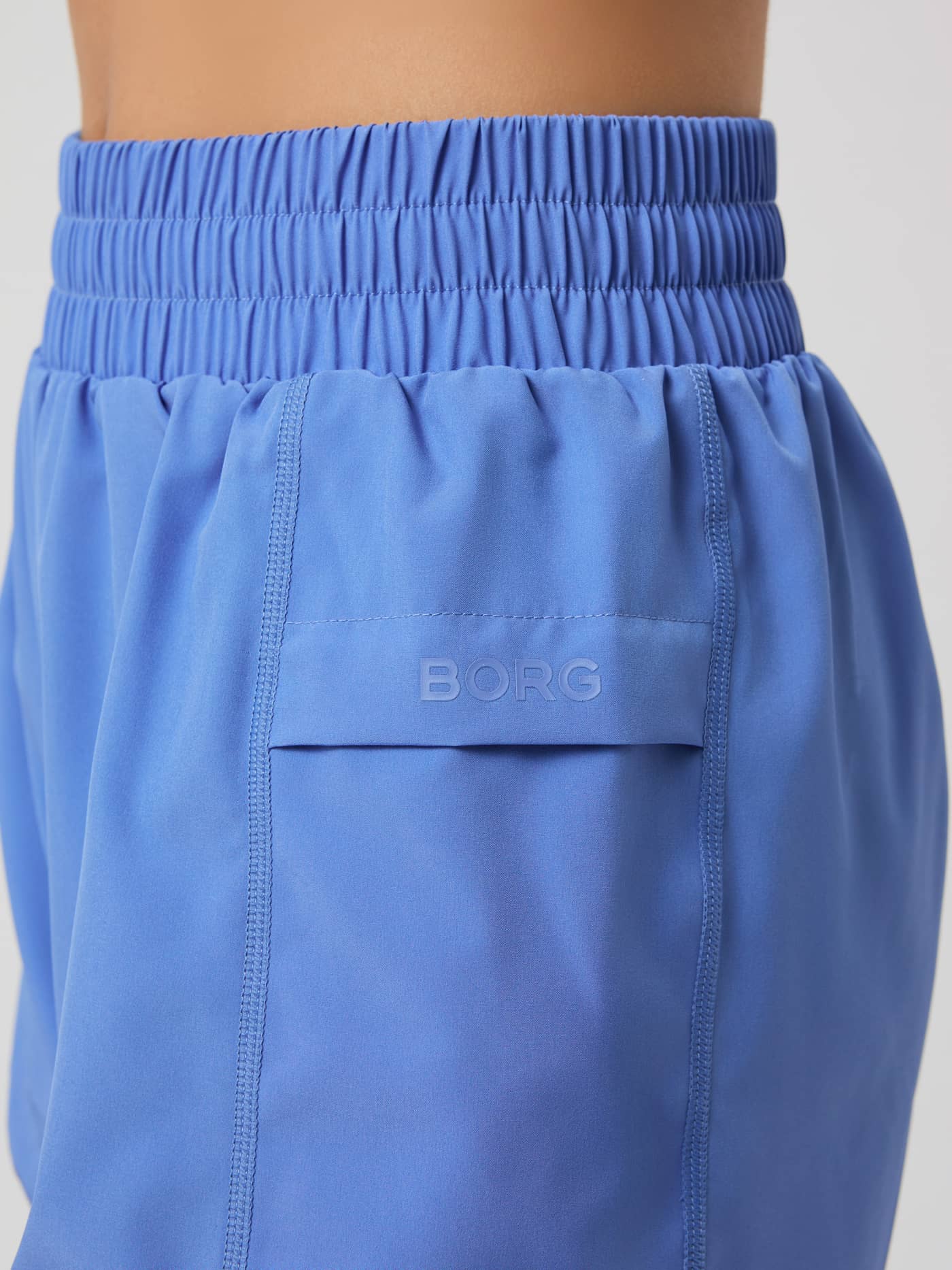Close-up of the Borg Loose Shorts in Ultramarine (Blue), showing the elastic waistband and side pocket with a logo. - Image 4