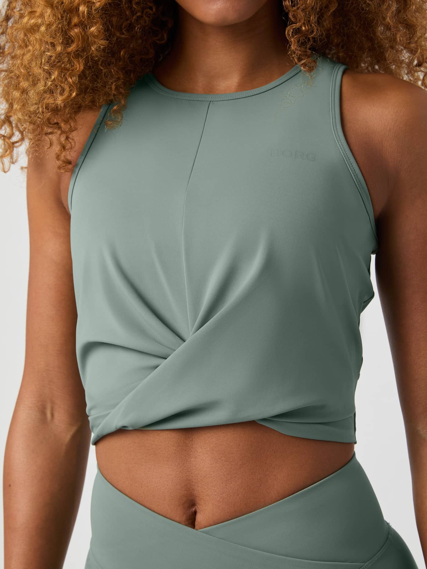 Front view of a woman wearing the Agave Green (Green) Studio Cross Tank Top with a twisted training fit and green logo. - Image 4