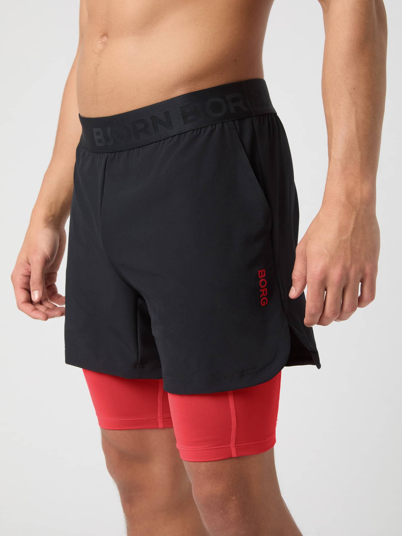 Side view of a man wearing Borg 2 In 1 Shorts in Black Beauty (Black) with red inner shorts and a red logo for training. - Image 1