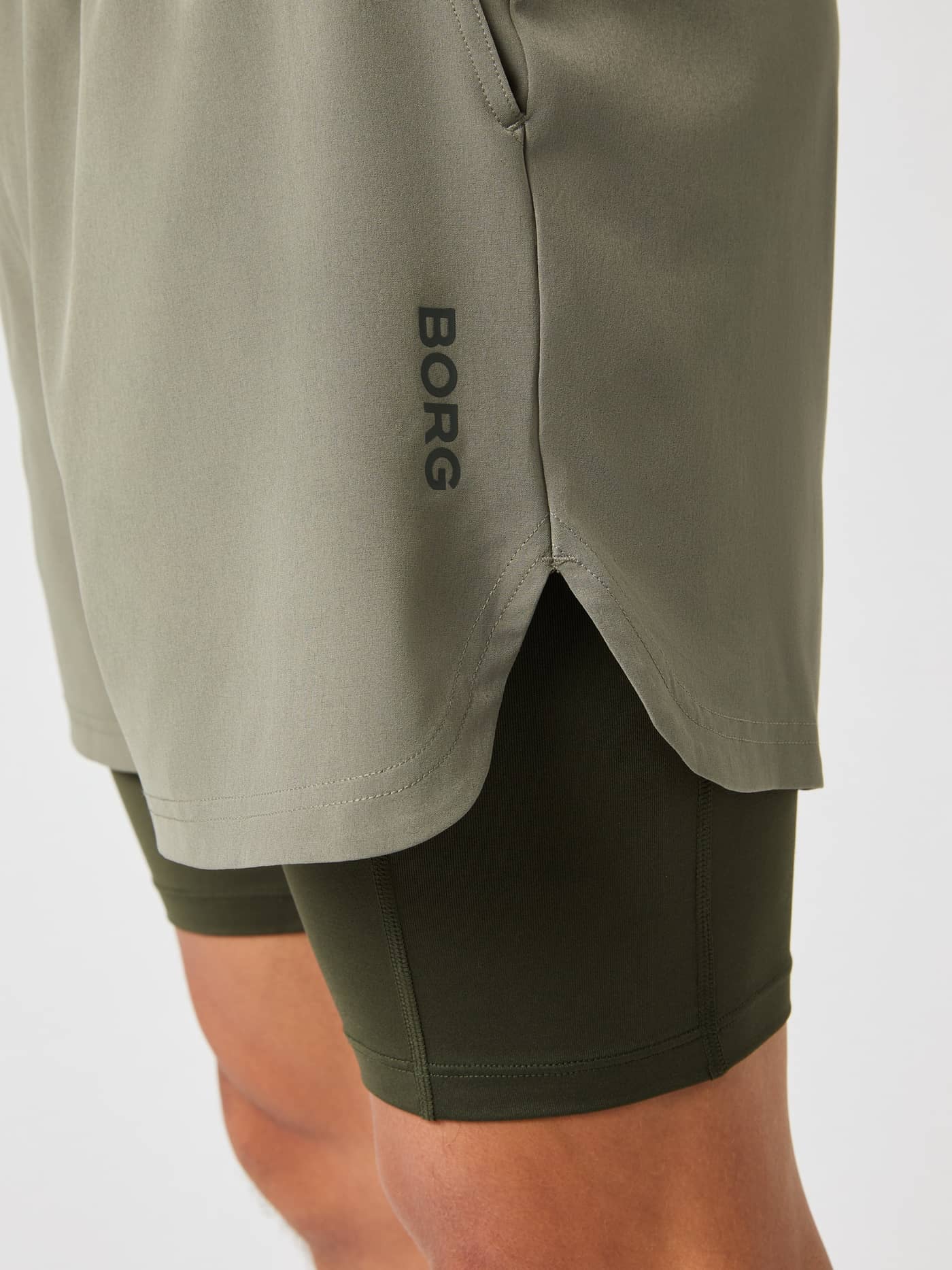 Detalle lateral de Borg 2 In 1 Shorts de hombre en Dusty Olive (Verde) con logo negro y pantalón interior de entrenamiento. - Image 3