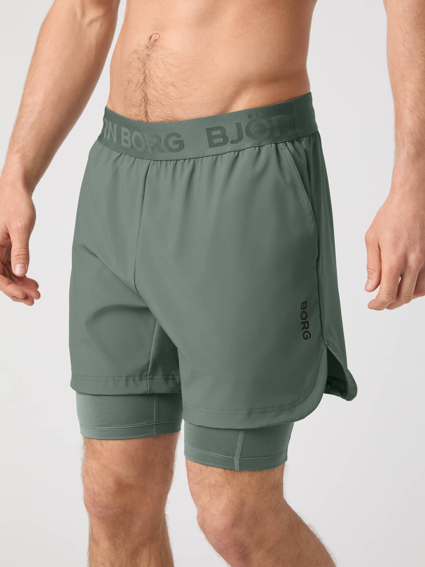 Front view of a man wearing the Agave Green (Green) Borg 2 In 1 Shorts with a black logo, built for training and running. - Image 1