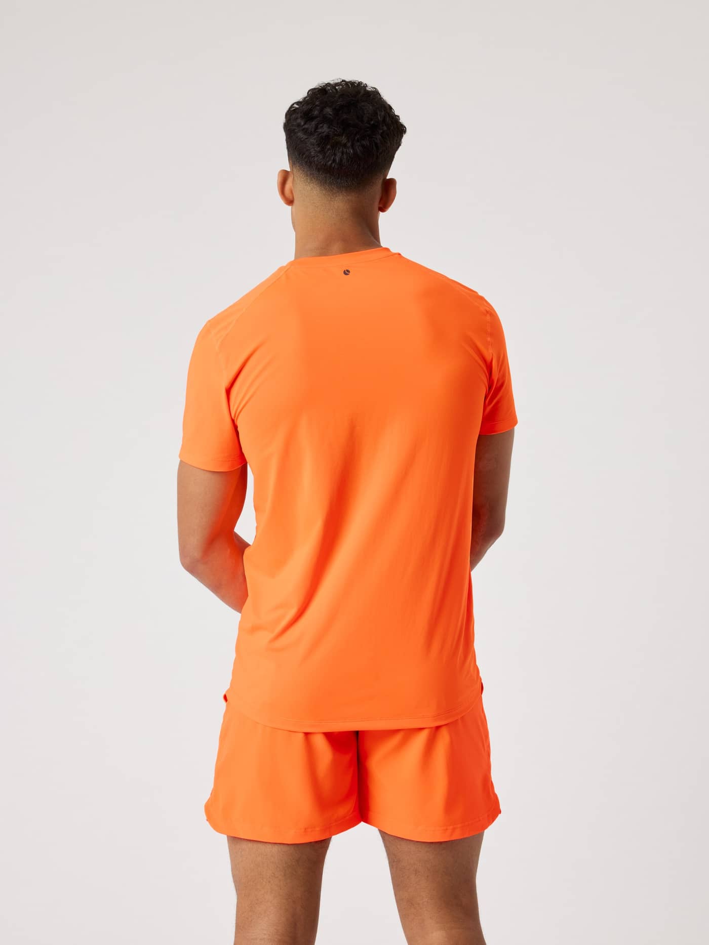 Back view of a man in the Borg Athletic T-Shirt in Shocking Orange (Orange), a performance training top with a dark logo. - Image 3