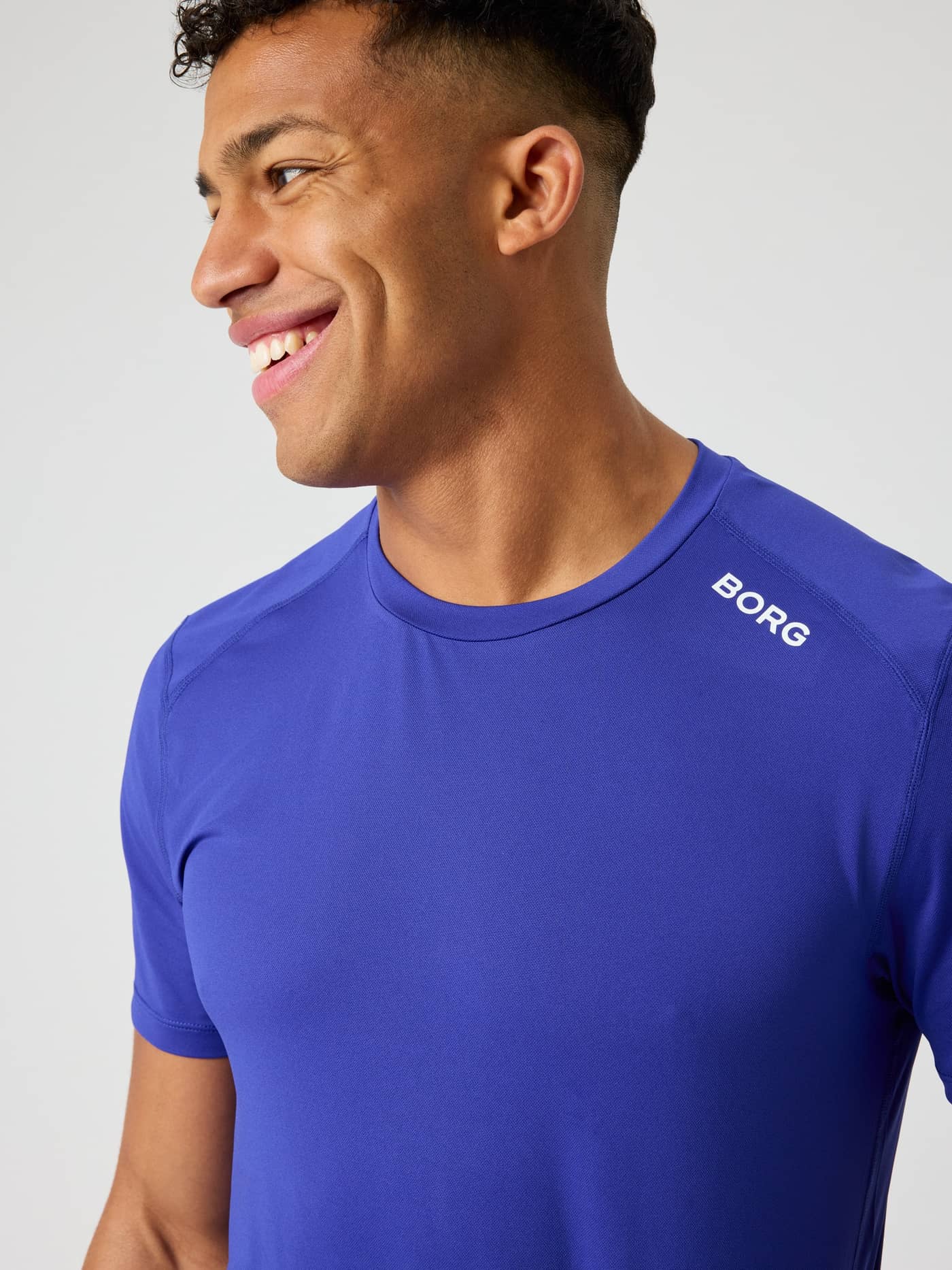 Närbild på en man i Borg Athletic T-Shirt i Clematis Blue (Blå) för träning med en vit logotyp på axeln. - Image 3