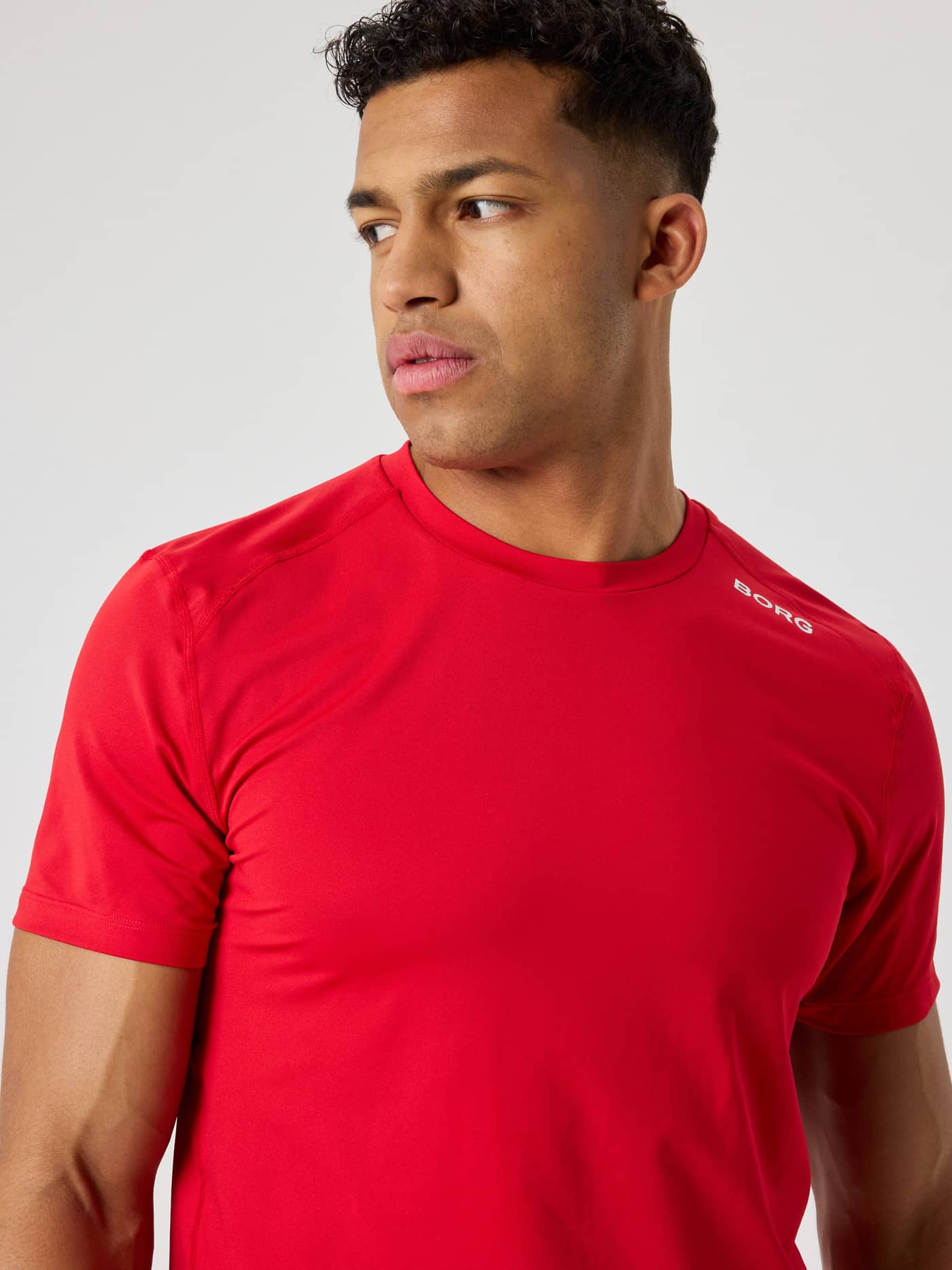 Front view of a man wearing the breathable Björn Borg Athletic T-Shirt in Lychee (Red) with a white logo for training. - Image 4