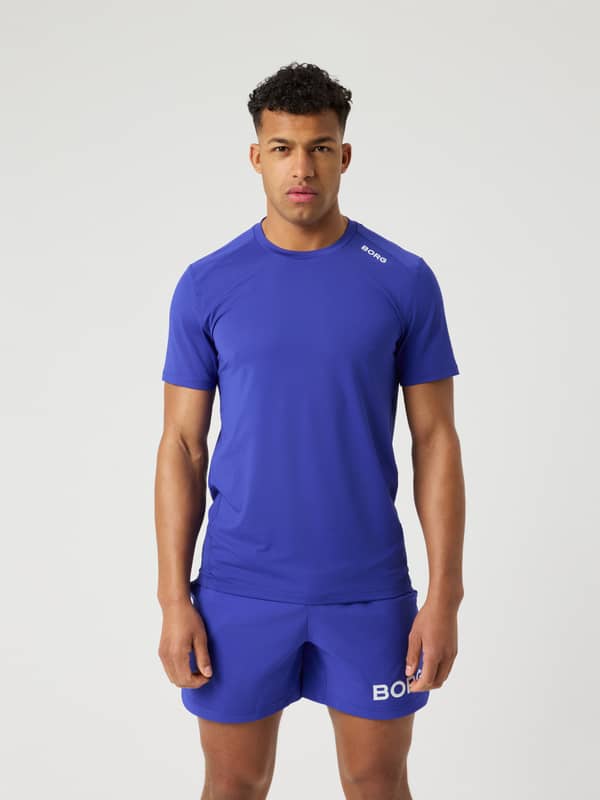 Framifrån på en man i stilren, funktionell Borg Athletic T-Shirt i Clematis Blue (Blå) med vit logotyp för träning.