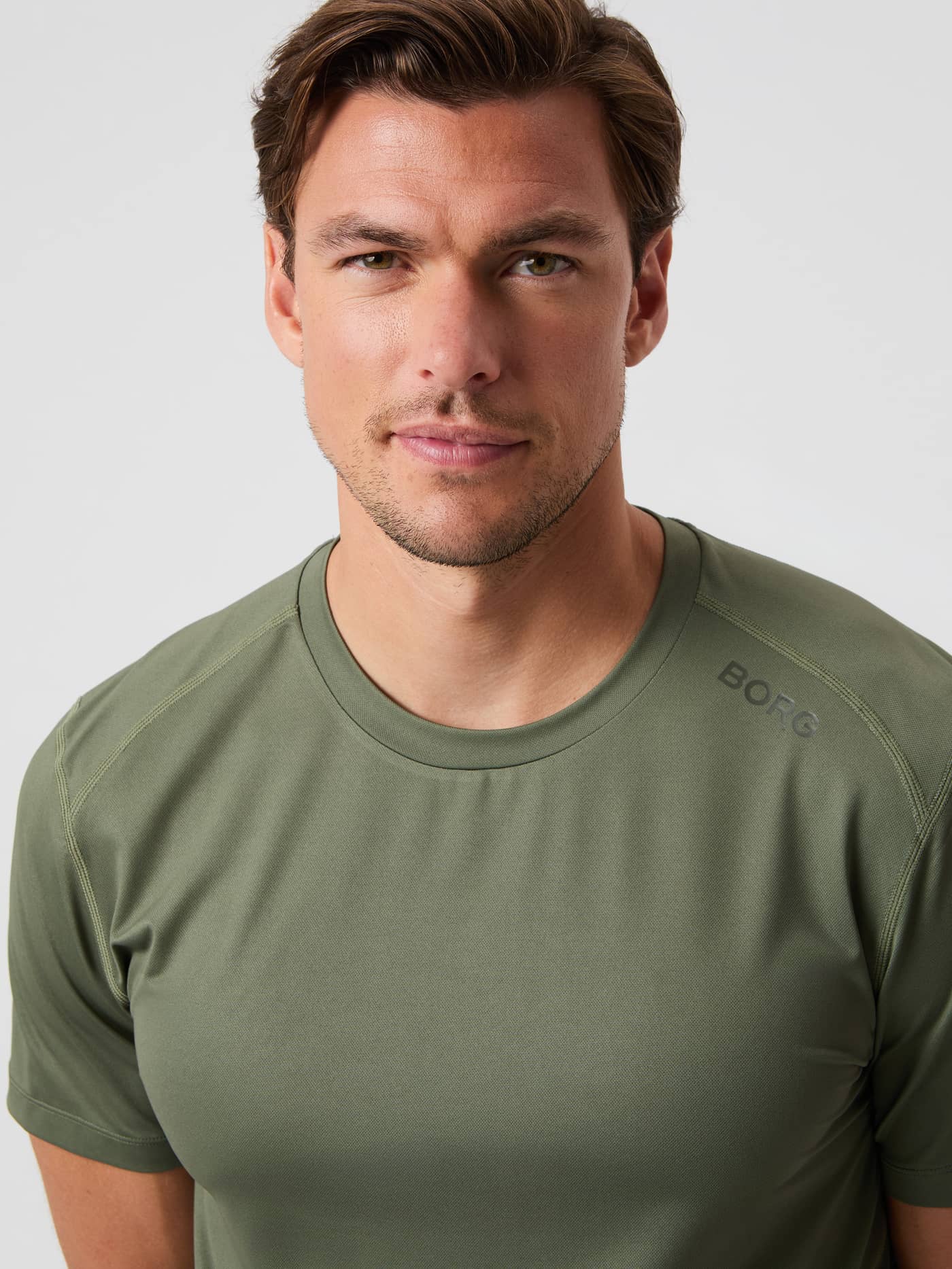 Närbild på en man i Borg Athletic T-Shirt i Thyme (Grön) med rund halsringning och en subtil logotyp för träning. - Image 5