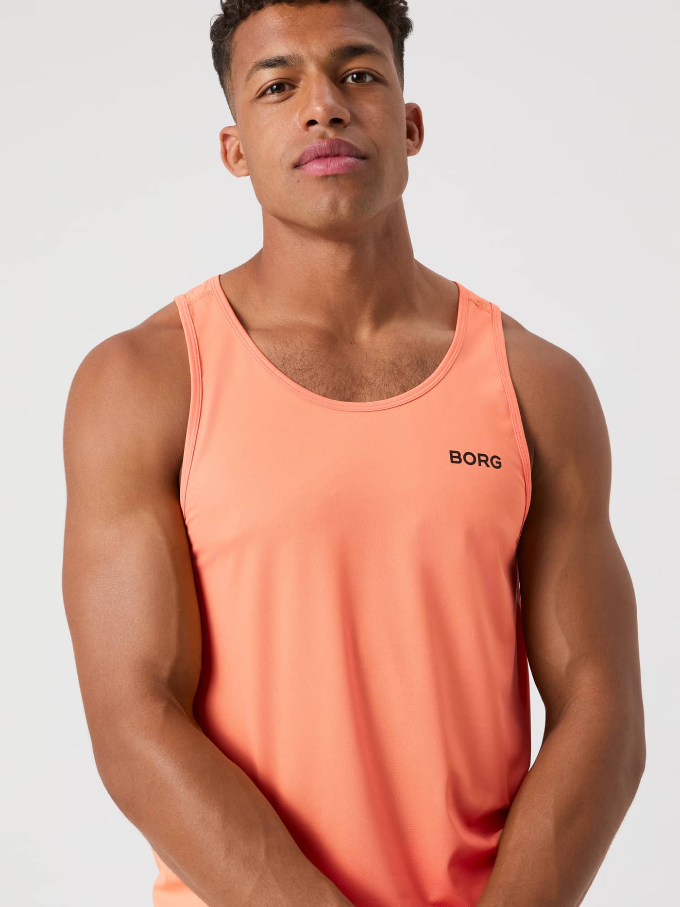 Vooraanzicht van een man in de Borg Athletic Tank in Papaya (Oranje), een ademende trainingstop met zwart logo. - Image 5