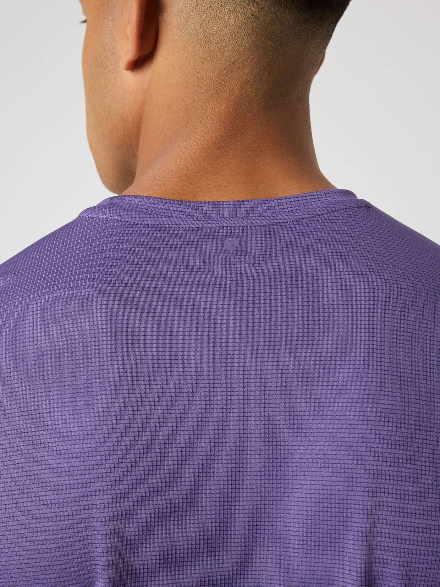 Back neck close-up of the Borg Light T-Shirt in Mystical (Purple) with a tonal tennis ball logo on structured fabric. - Image 4