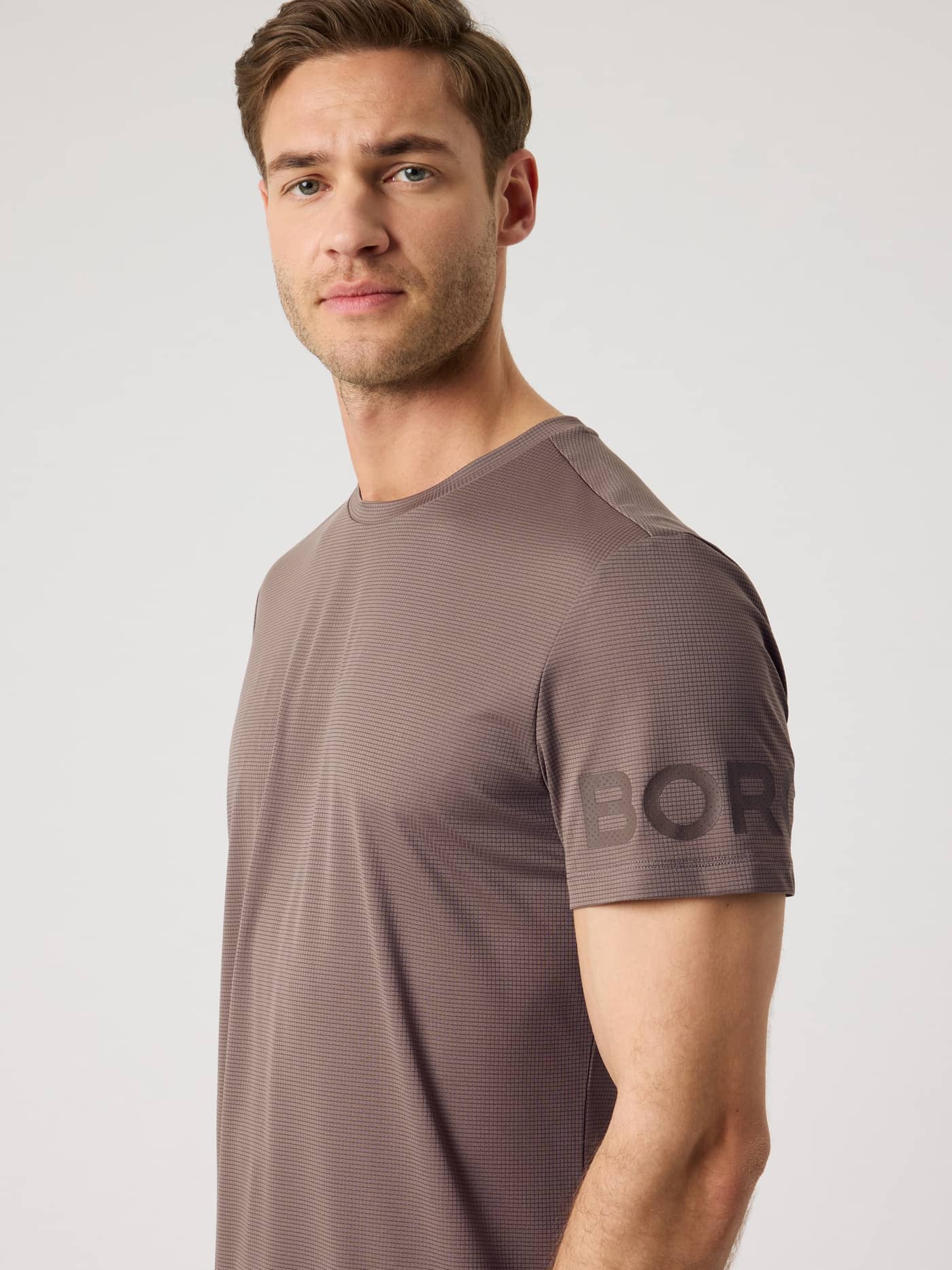 Zijaanzicht van een model in het Björn Borg Light T-Shirt in Falcon (Bruin) met donker logo op de mouw voor training. - Image 5