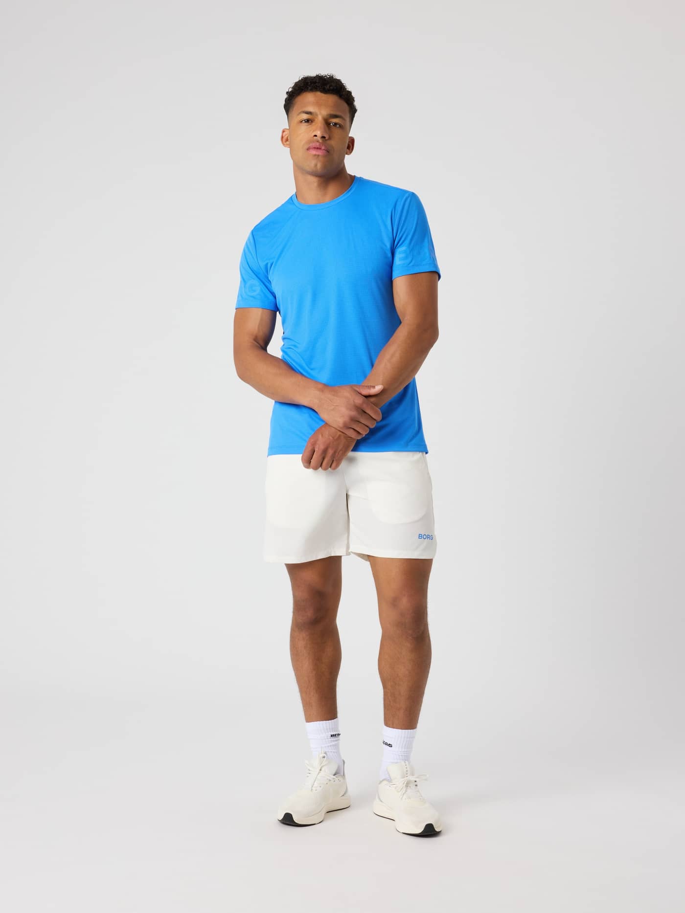 Full-body front view of a man wearing the Palace Blue (Blue) Borg Light T-Shirt, a functional training tee with sleeve logos. - Image 3