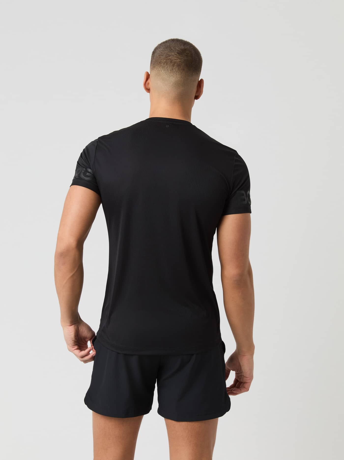 Achteraanzicht van een man in de Borg Light T-Shirt in Black Beauty (Zwart) voor training en tennis met mouwprints. - Image 2