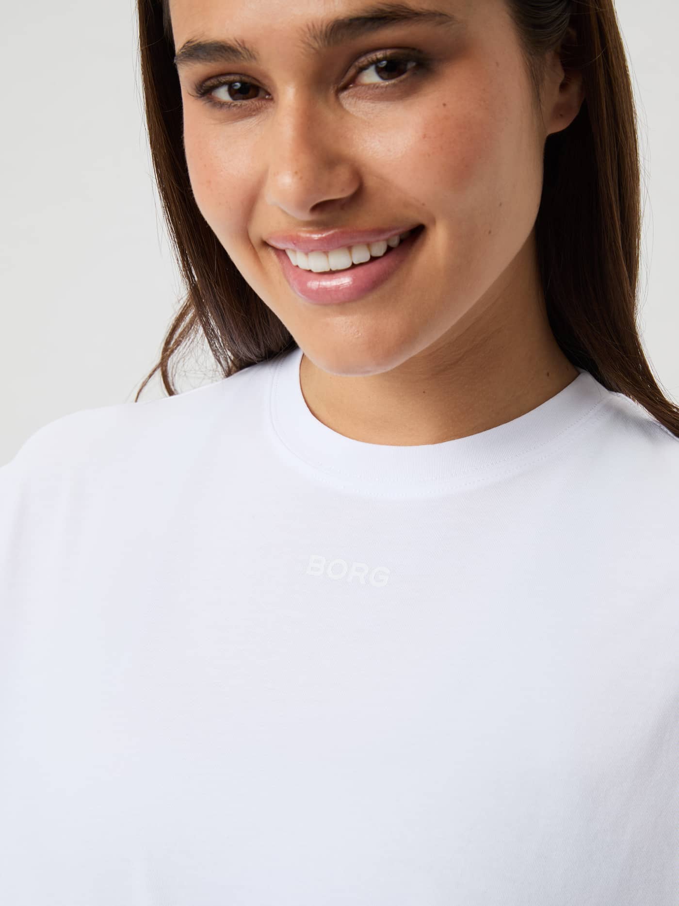 Gros plan d'une femme portant le Studio Oversized T-Shirt Brilliant White (Blanc) avec logo blanc discret sur la poitrine. - Image 2