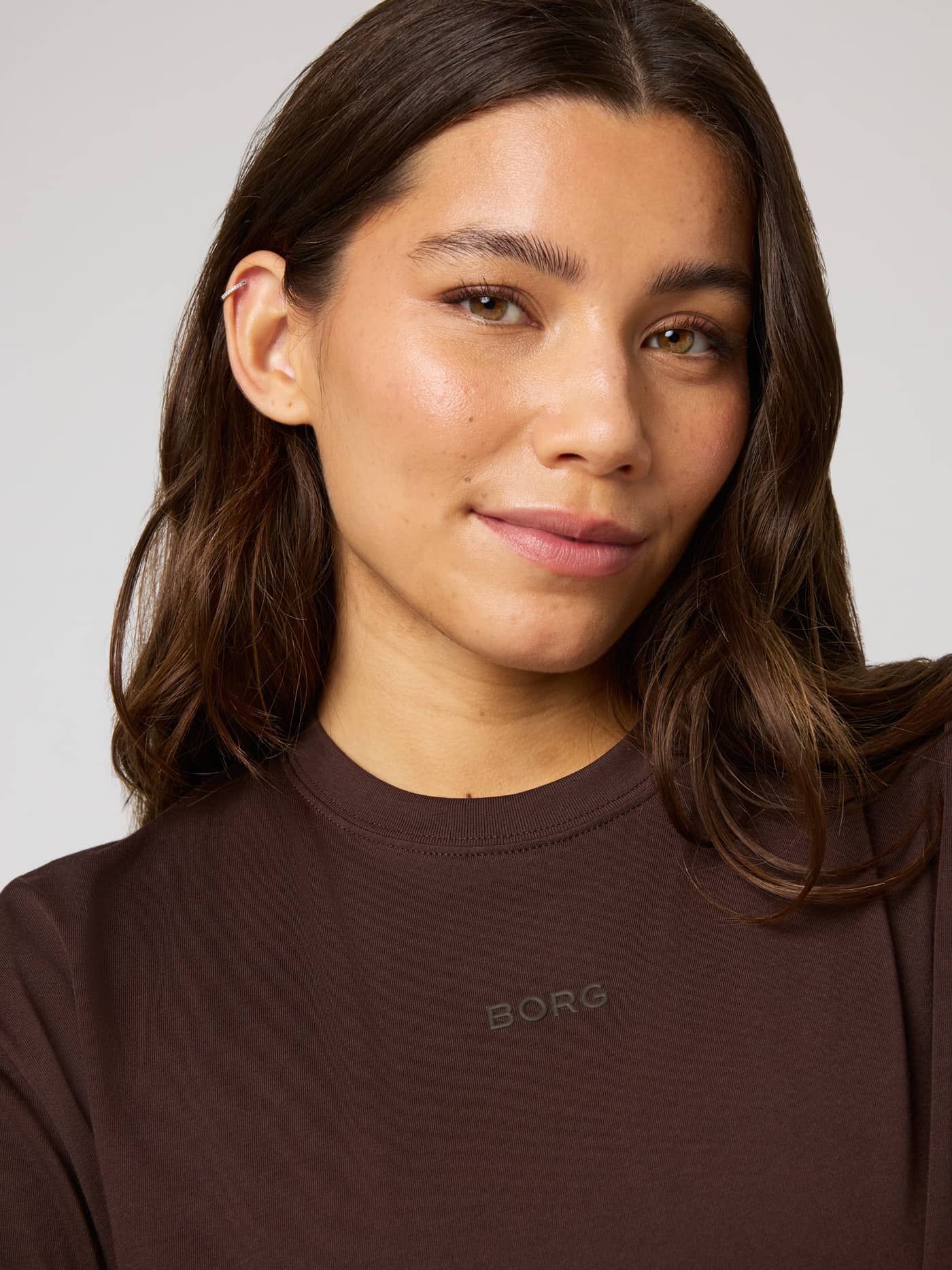 Close-up of a model in the Studio Oversized T-Shirt in Coffee Bean (Brown) featuring a matching Borg logo on the chest. - Image 5