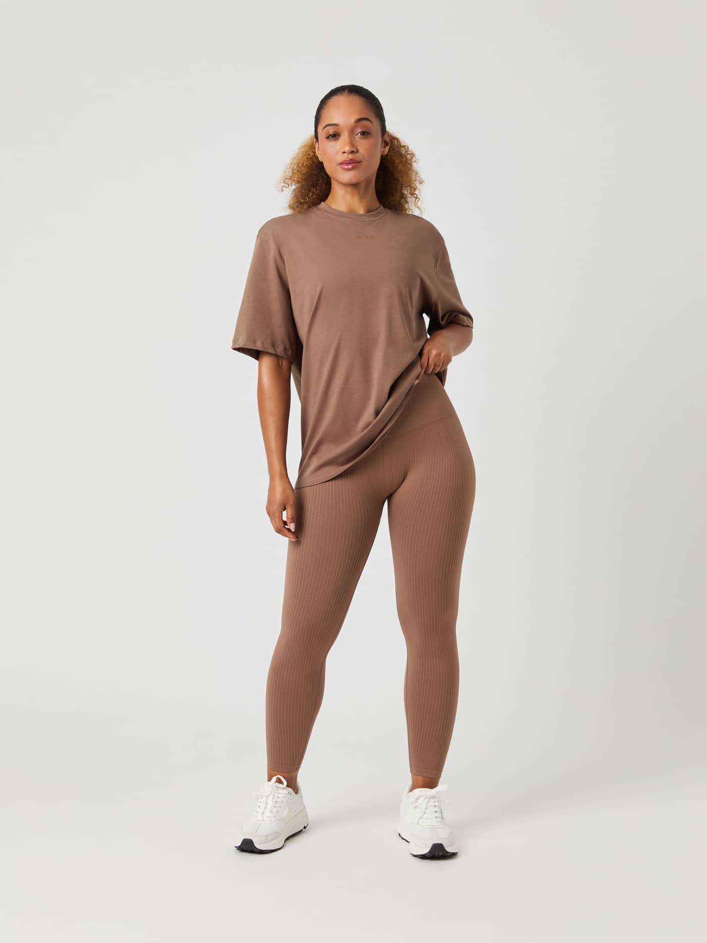 Vue de face d'un mannequin portant le Studio Oversized T-Shirt en Acorn (Marron), legging assorti et baskets blanches. - Image 3