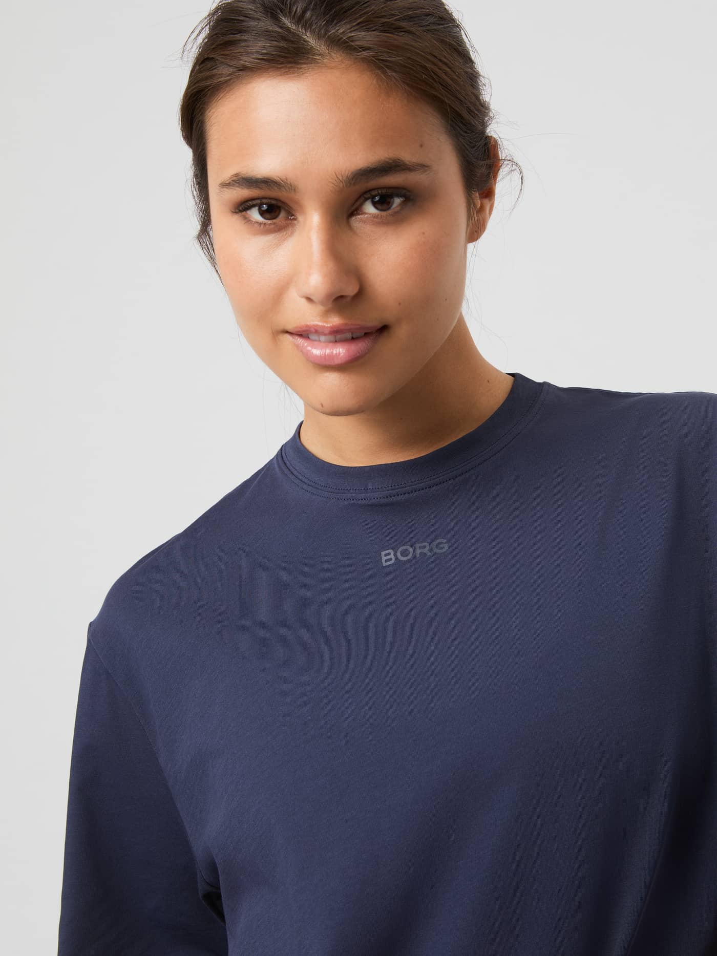 Närbild på en modell i Studio Oversized T-Shirt i Odyssey Gray (Grå) med en grå logotyp på bröstet. - Image 4
