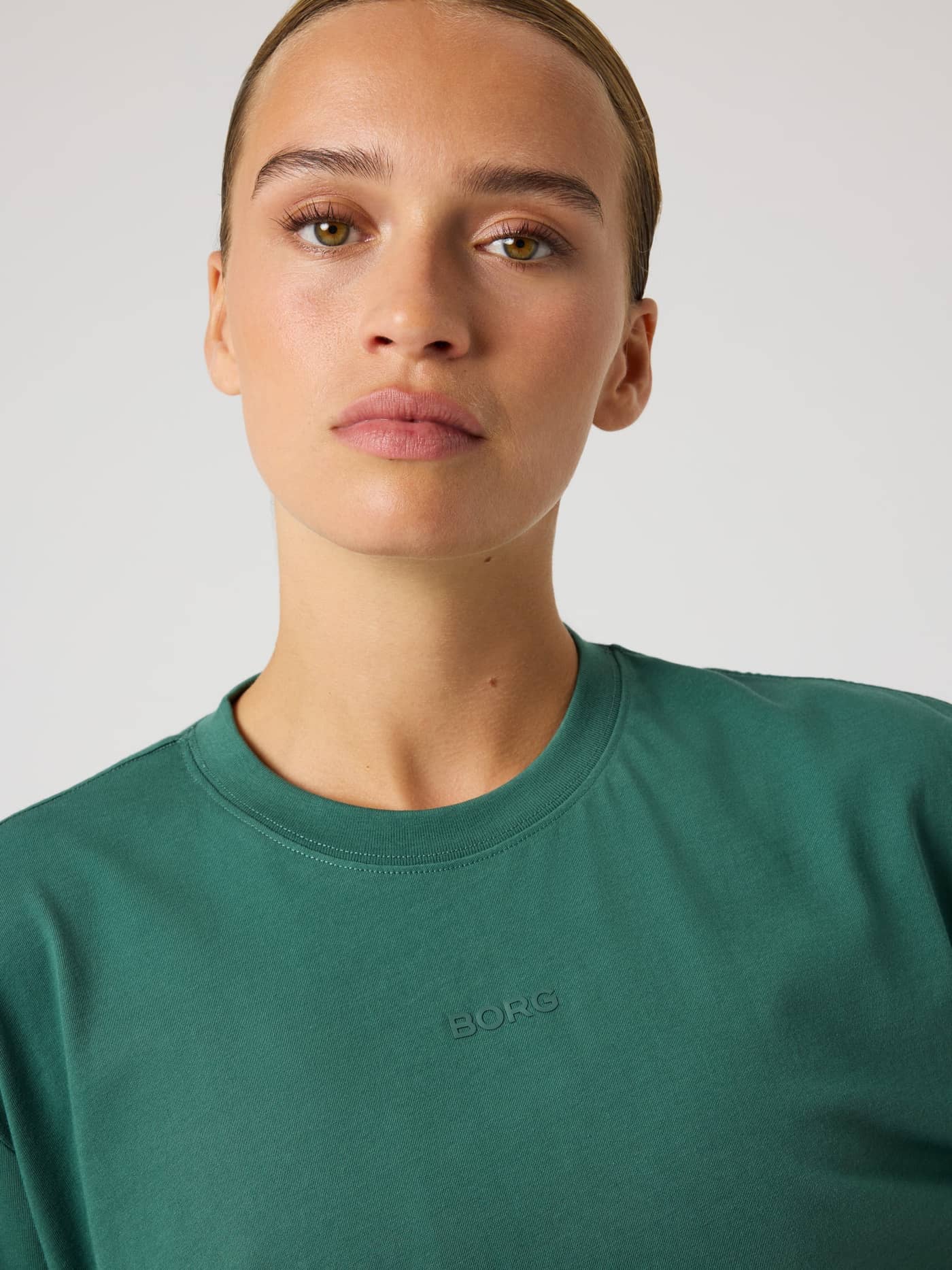 Close-up of a woman in the Mallard Green (Green) Studio Oversized T-Shirt, a loose training tee with a green BORG logo. - Image 4
