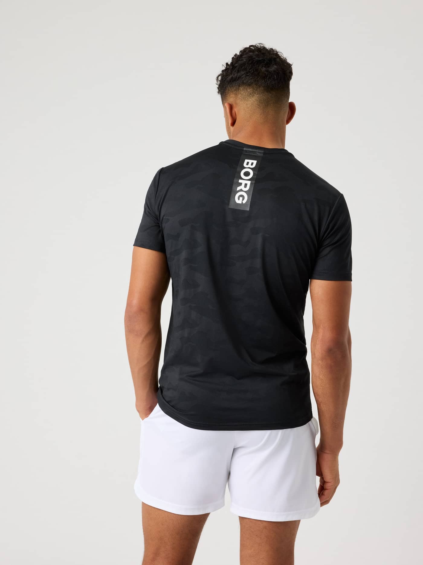 Rückansicht eines Mannes im Camo Borg Performance T-Shirt in Black Beauty (Schwarz) mit weißem Logo für Training und Tennis. - Image 2