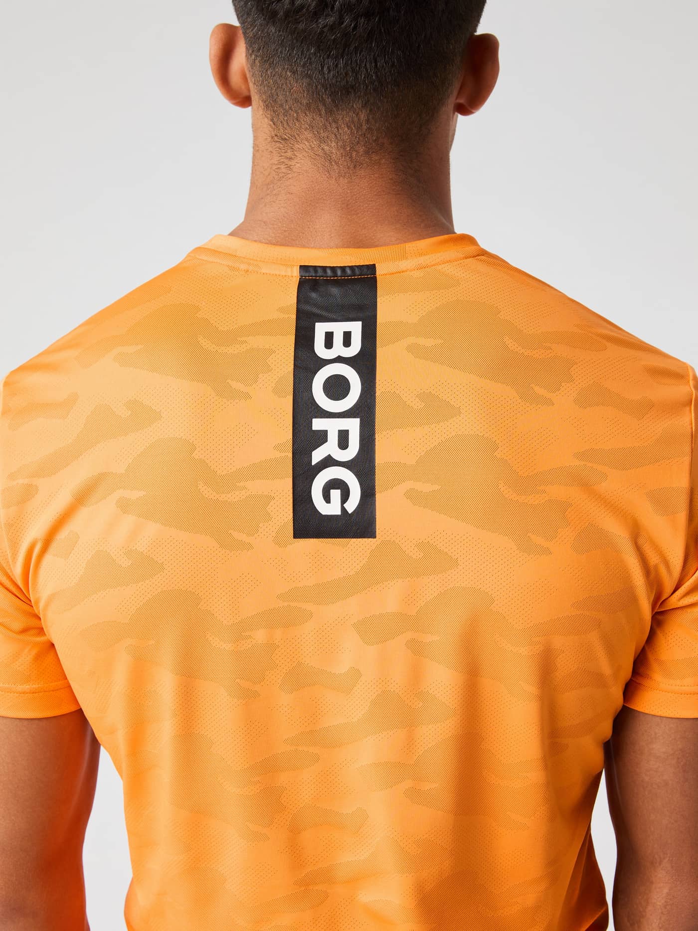 Rückansicht eines Mannes im Sun Orange (Orange) Borg Performance T-Shirt zum Training mit Camo-Print und weißem BORG-Logo. - Image 5