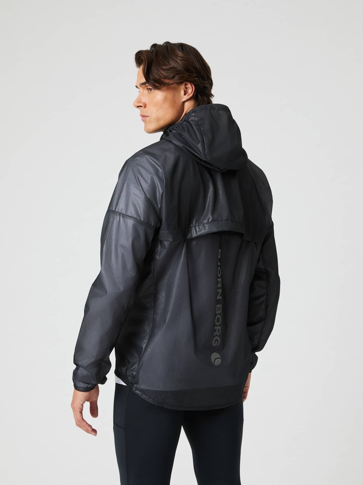Rückansicht eines Mannes in der Borg Performance Jacket in Black Beauty (Schwarz), Laufjacke mit Kapuze und grauem Logo. - Image 2