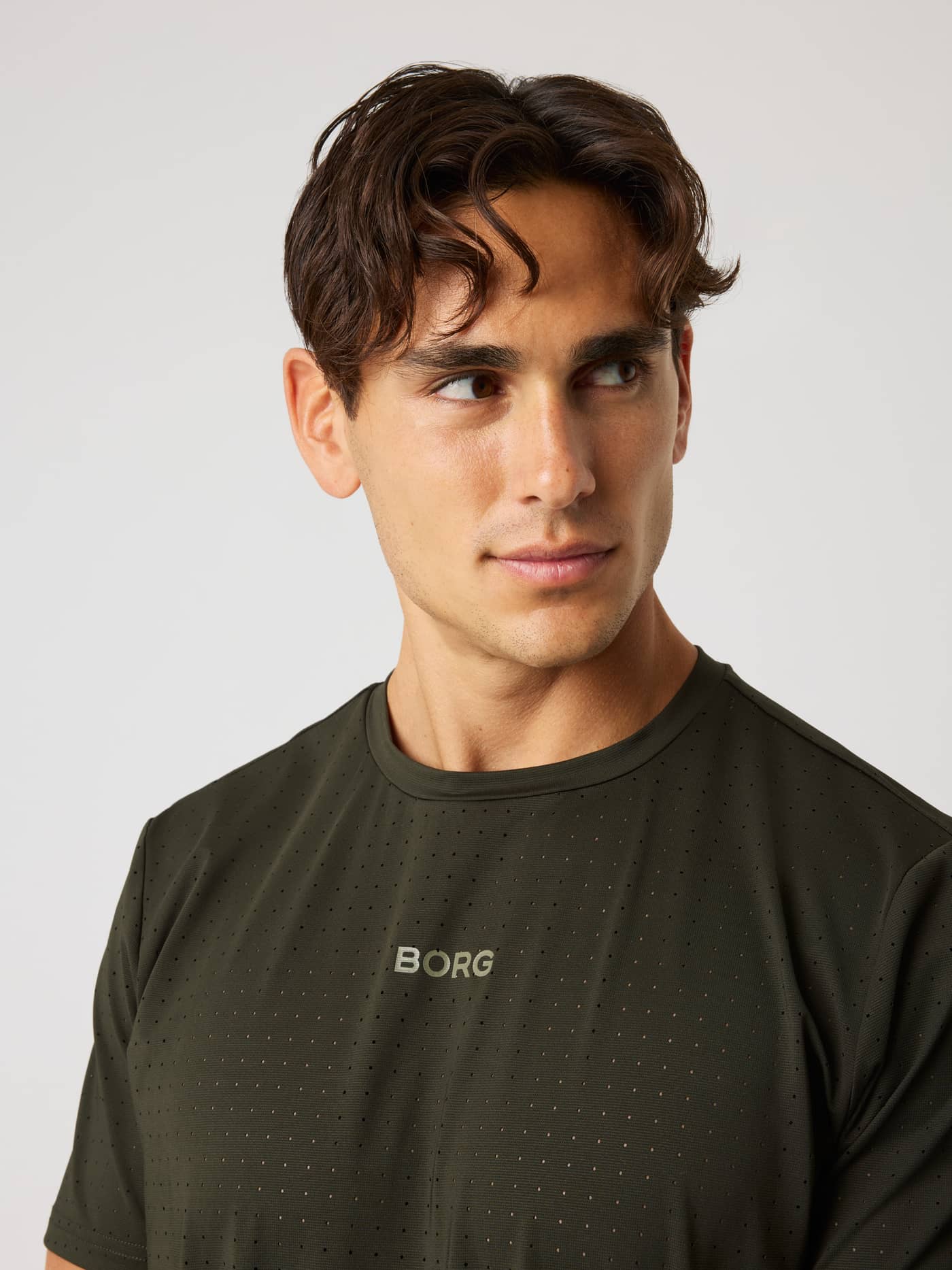 Close-up of a man in the Borg Performance Perforated T-Shirt in Rosin (Green) with a grey logo and running fabric. - Image 4