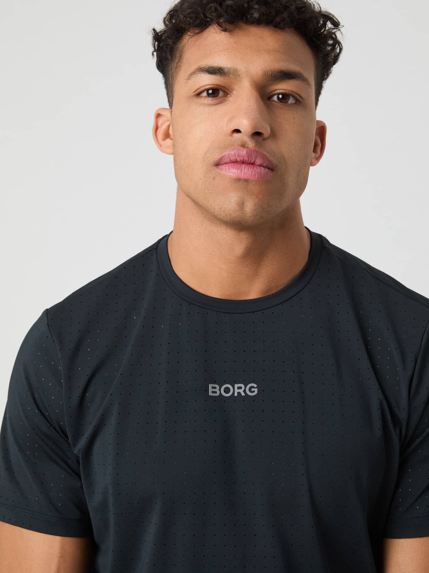 Close-up of a man wearing the Borg Performance Perforated T-Shirt in Black Beauty (Black) for running with a grey logo. - Image 5