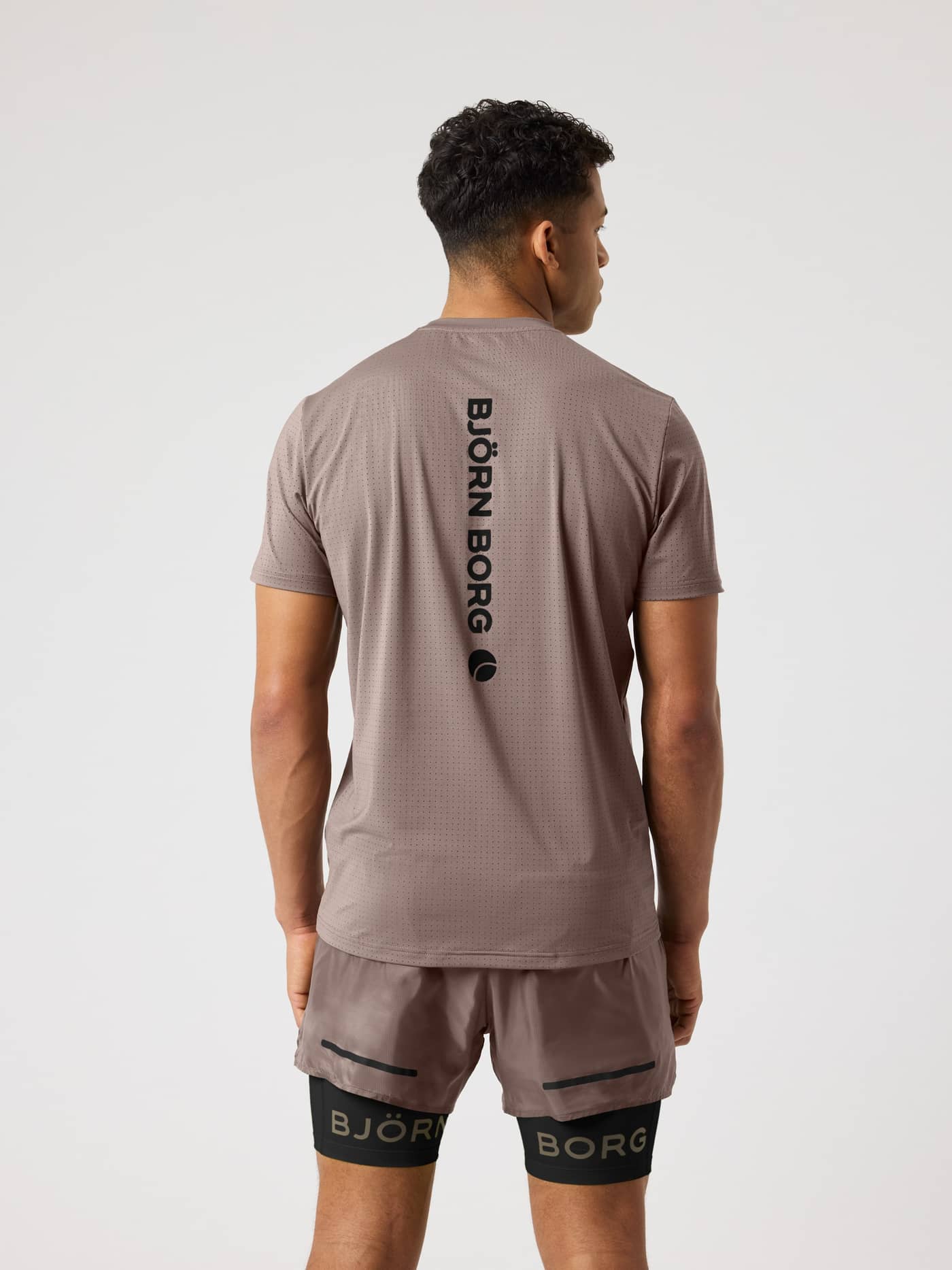 Achteraanzicht van een man in het Borg Running Perforated T-Shirt in Falcon (Bruin) met een verticaal zwart logo. - Image 2
