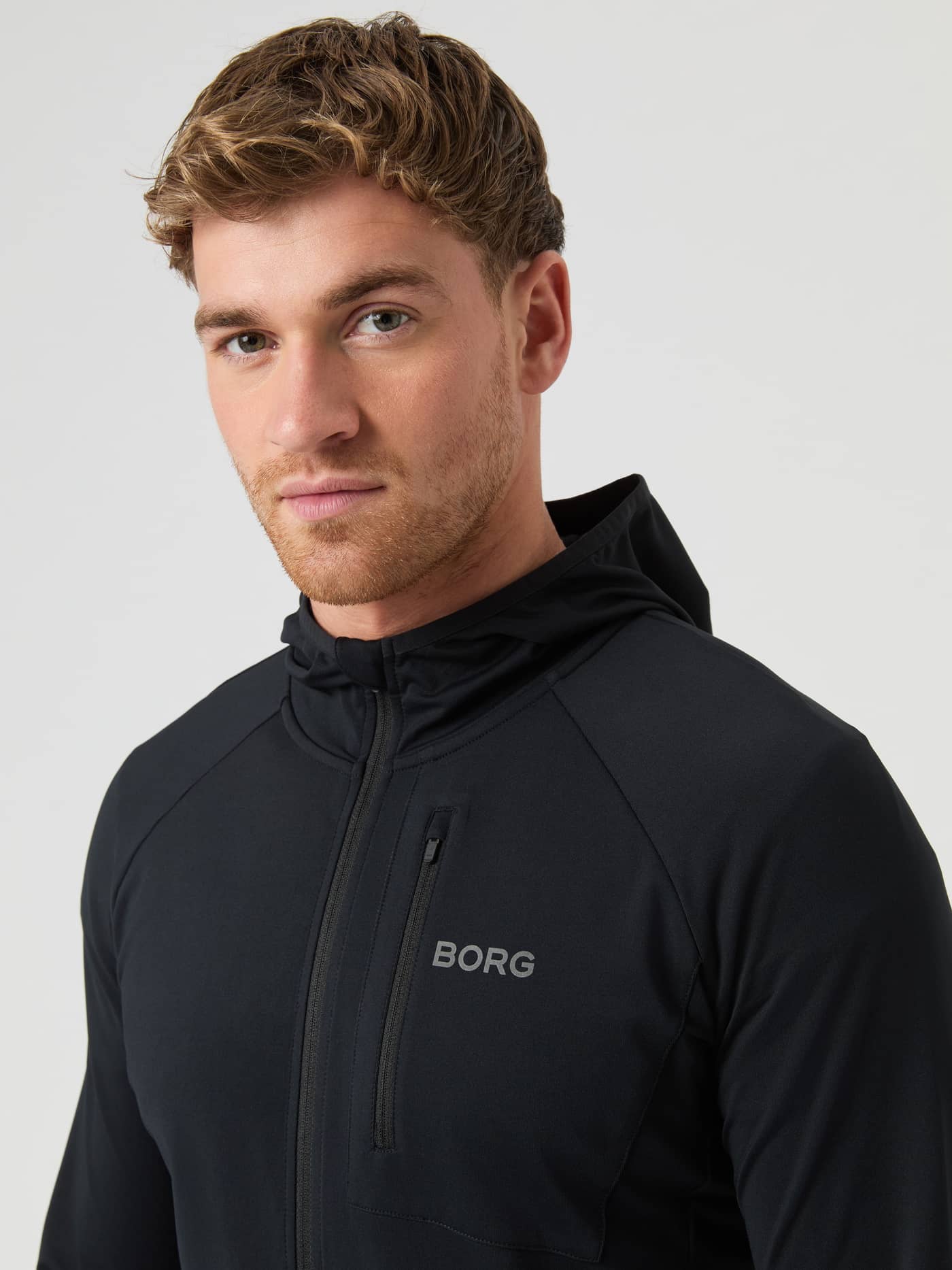 Front view of a man in the Björn Borg Running Mid Layer Hood in Black Beauty (Black) with a grey reflective logo for running. - Image 6