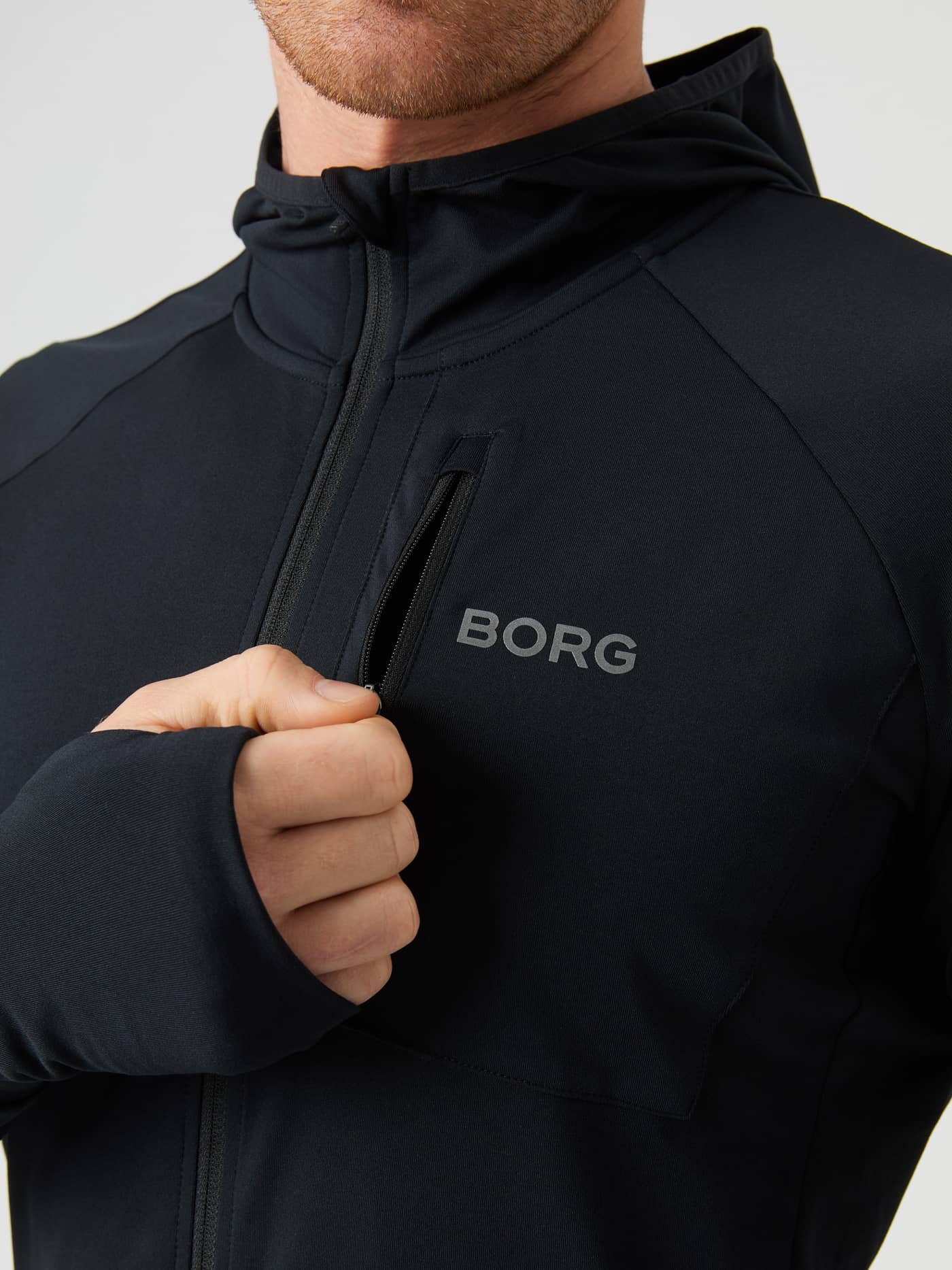 Close-up of the Borg Running Mid Layer Hood in Black Beauty (Black) featuring a grey logo and functional zipper pocket. - Image 4