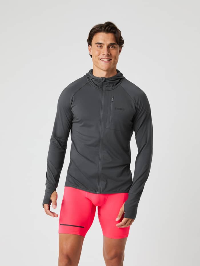 Vooraanzicht van man in de Borg Performance Mid Layer Hood in Asphalt (Grijs) met zwart logo en duimgaten voor hardlopen. - Image 2