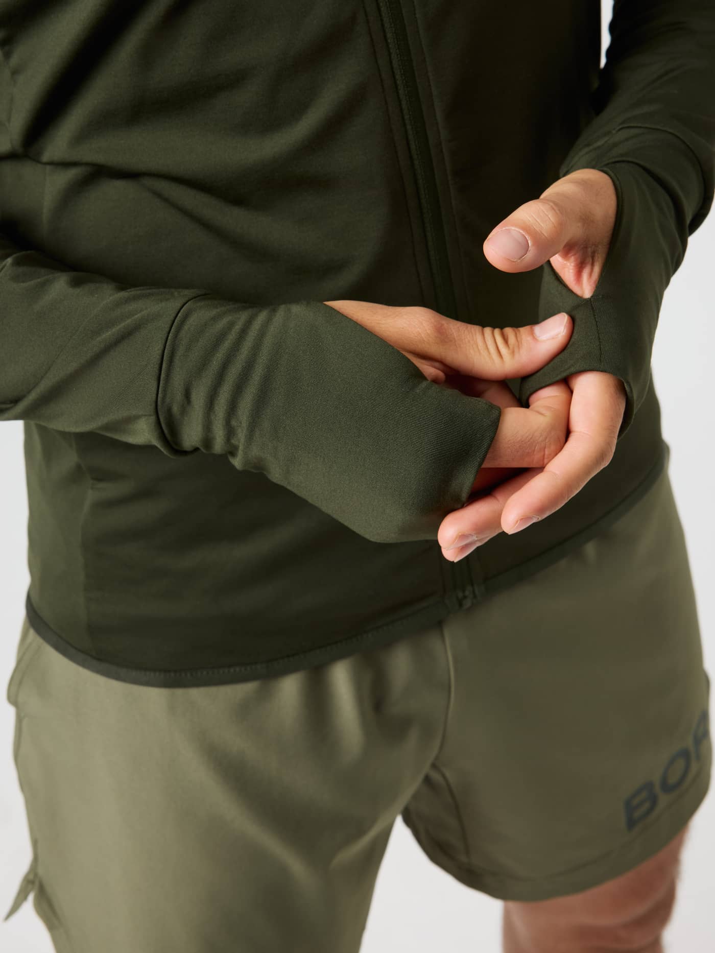 Close-up of the thumbholes on the Borg Performance Mid Layer Hood in Rosin (Green) for a functional running fit. - Image 5