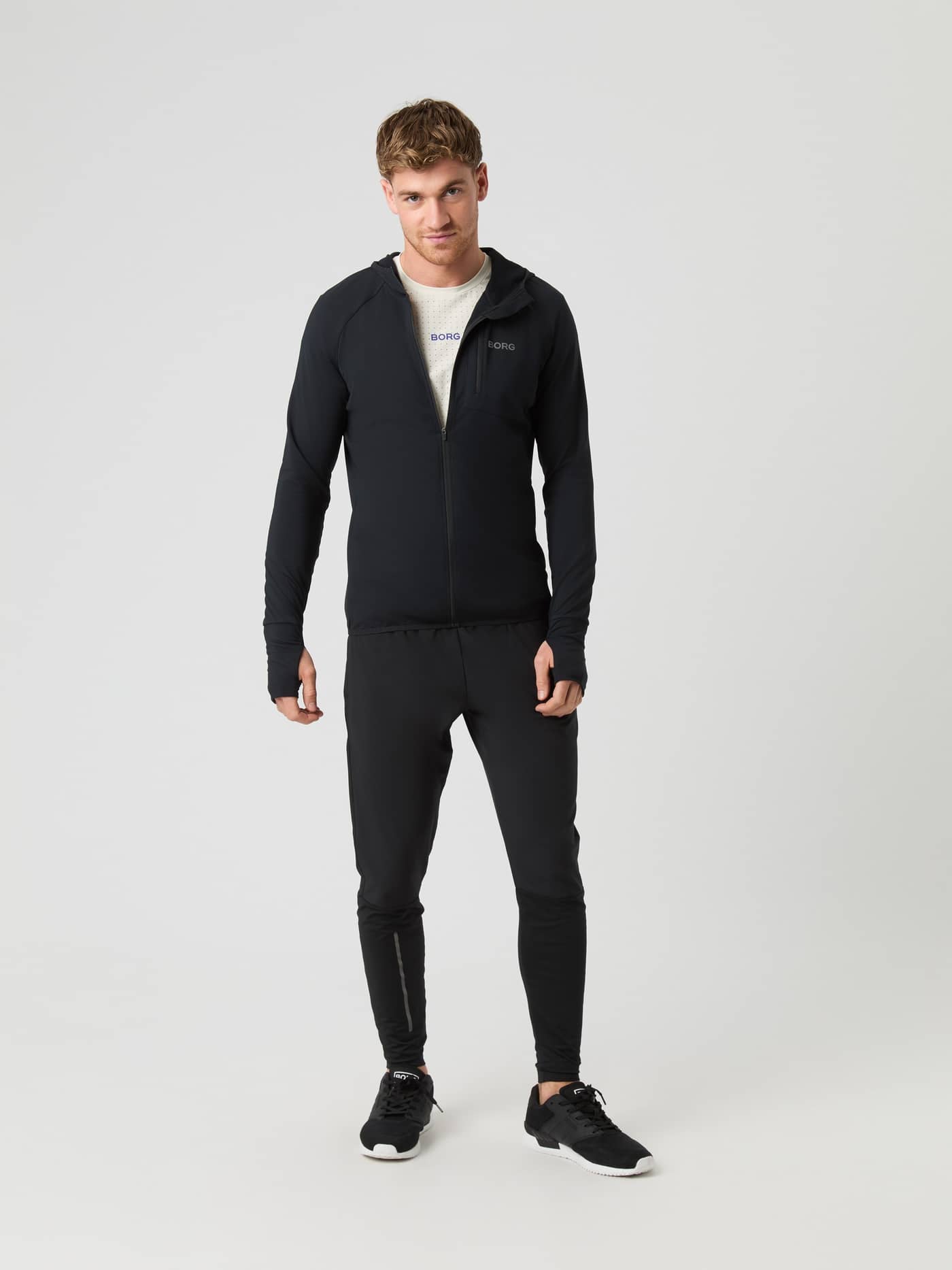 Full-body front view of a man wearing the Borg Running Mid Layer Hood in Black Beauty (Black) with reflective logo details. - Image 3