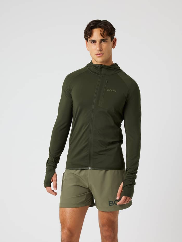 Front view of a model wearing the Borg Performance Mid Layer Hood in Rosin (Green) for running with a tonal logo.