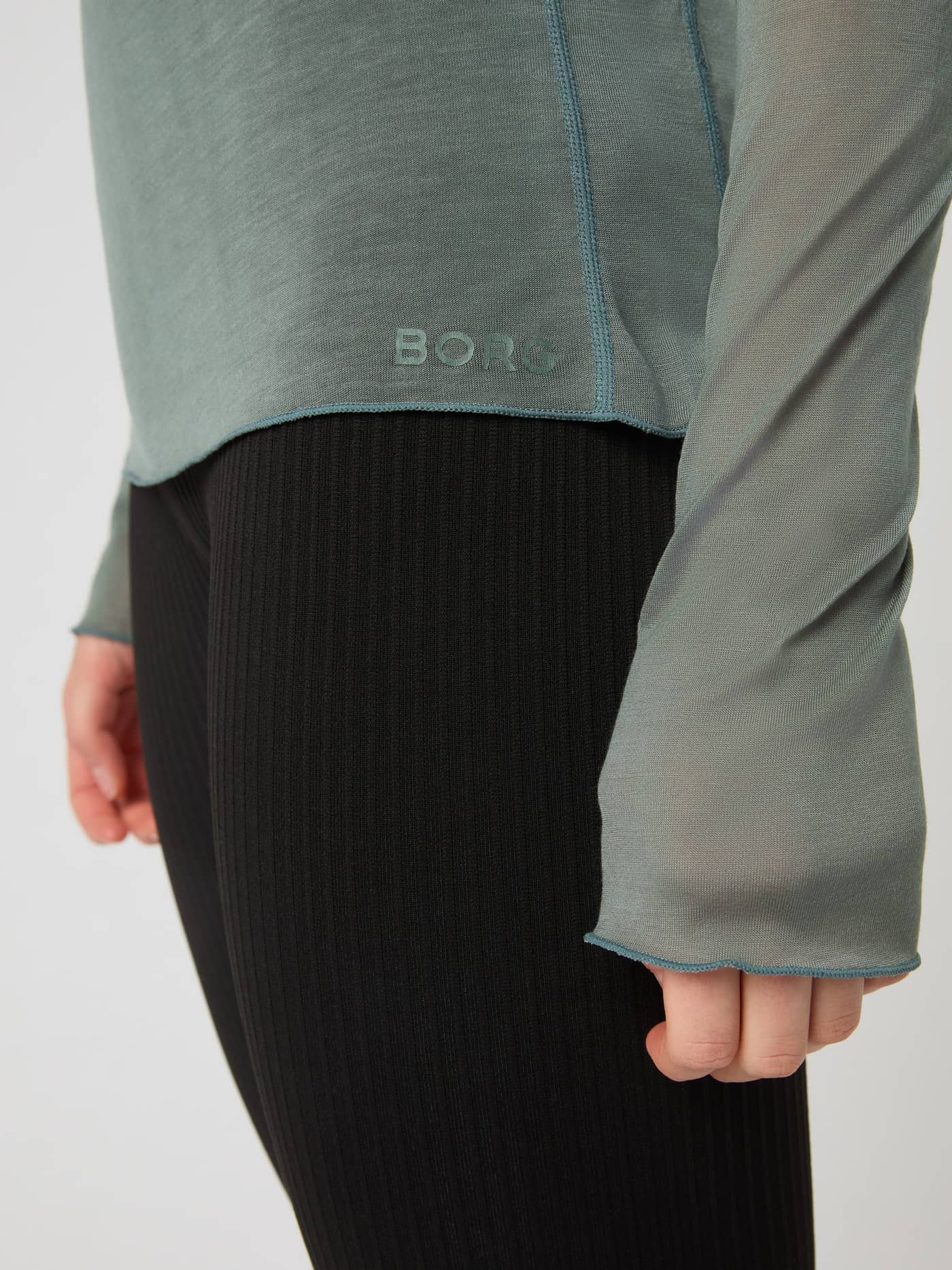 Close-up of the Studio Light Long Sleeve Top in Agave Green, showing the hem logo and sleeve cuff. - Image 5