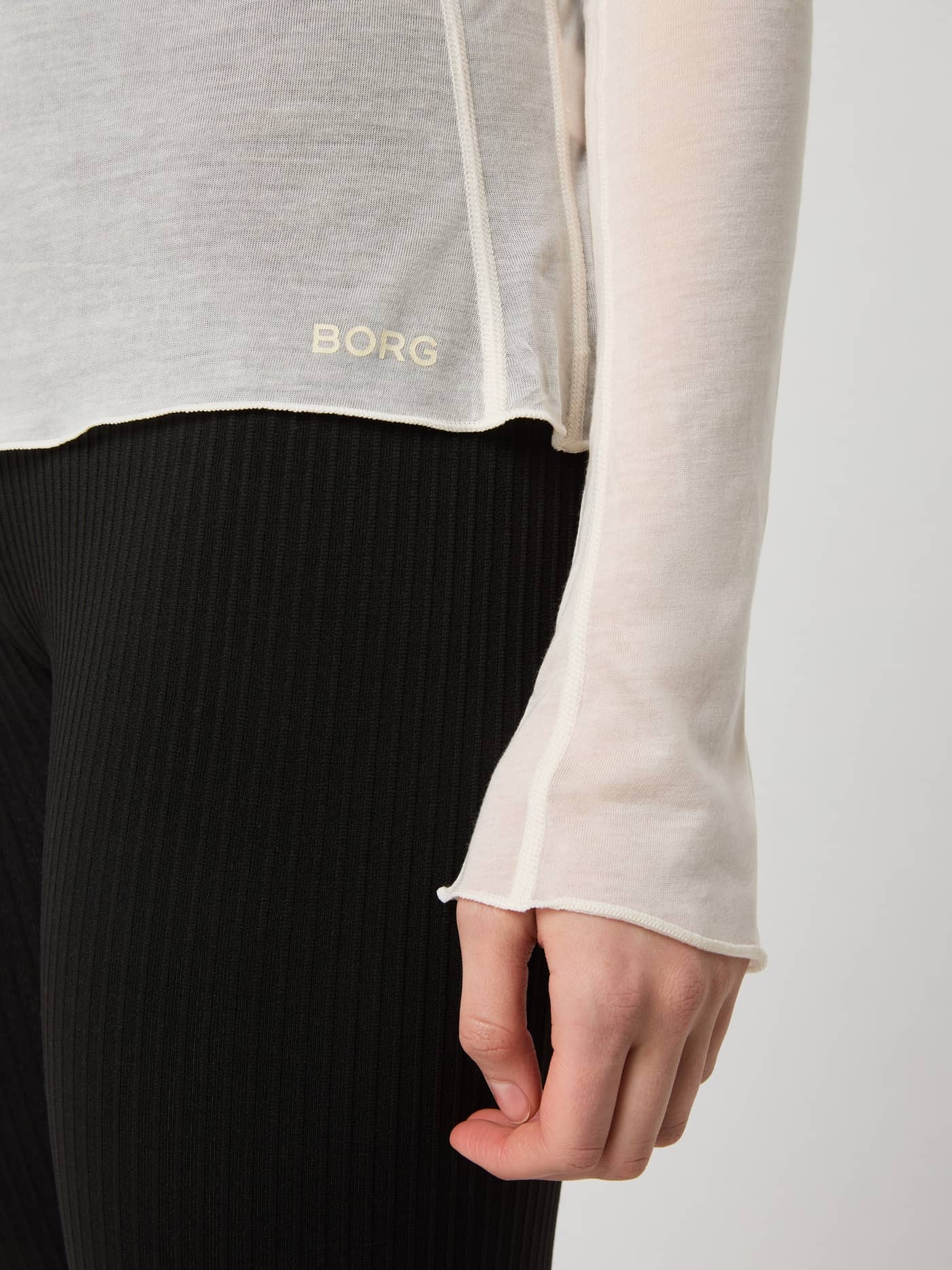 Detailed close-up of the Studio Light Long Sleeve Top in birch, showcasing the BORG logo on the hem and the sleeve cuff. - Image 5